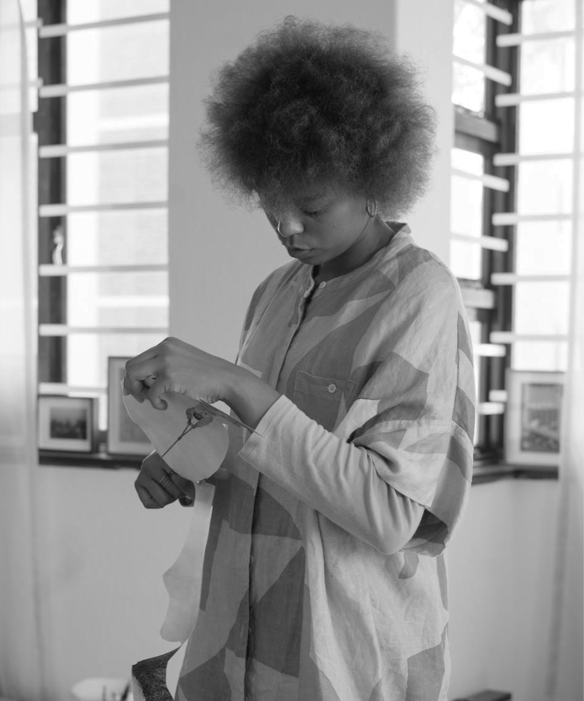 A woman with natural afro hair looking down and holding a photograph in her hands in a softly lit indoor space.