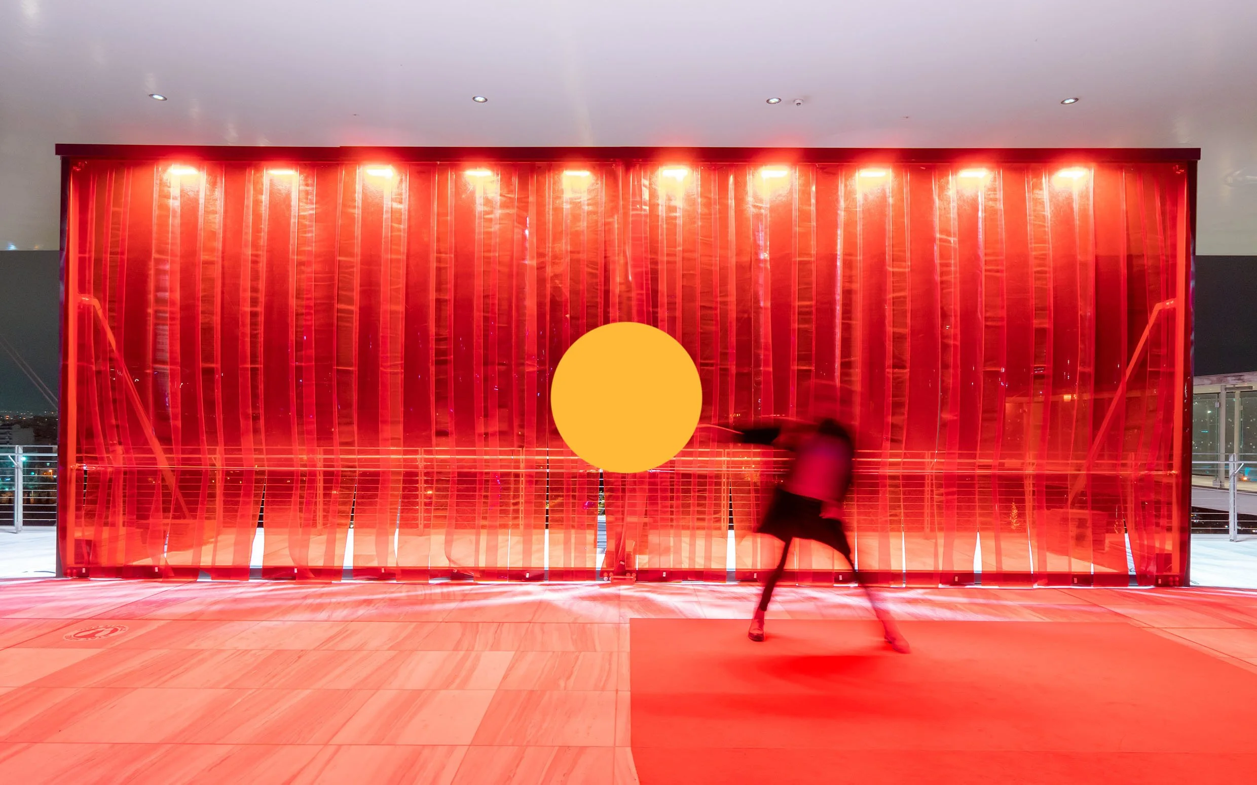Person running in front of an illuminated red modern art installation with a large yellow circle in the center.