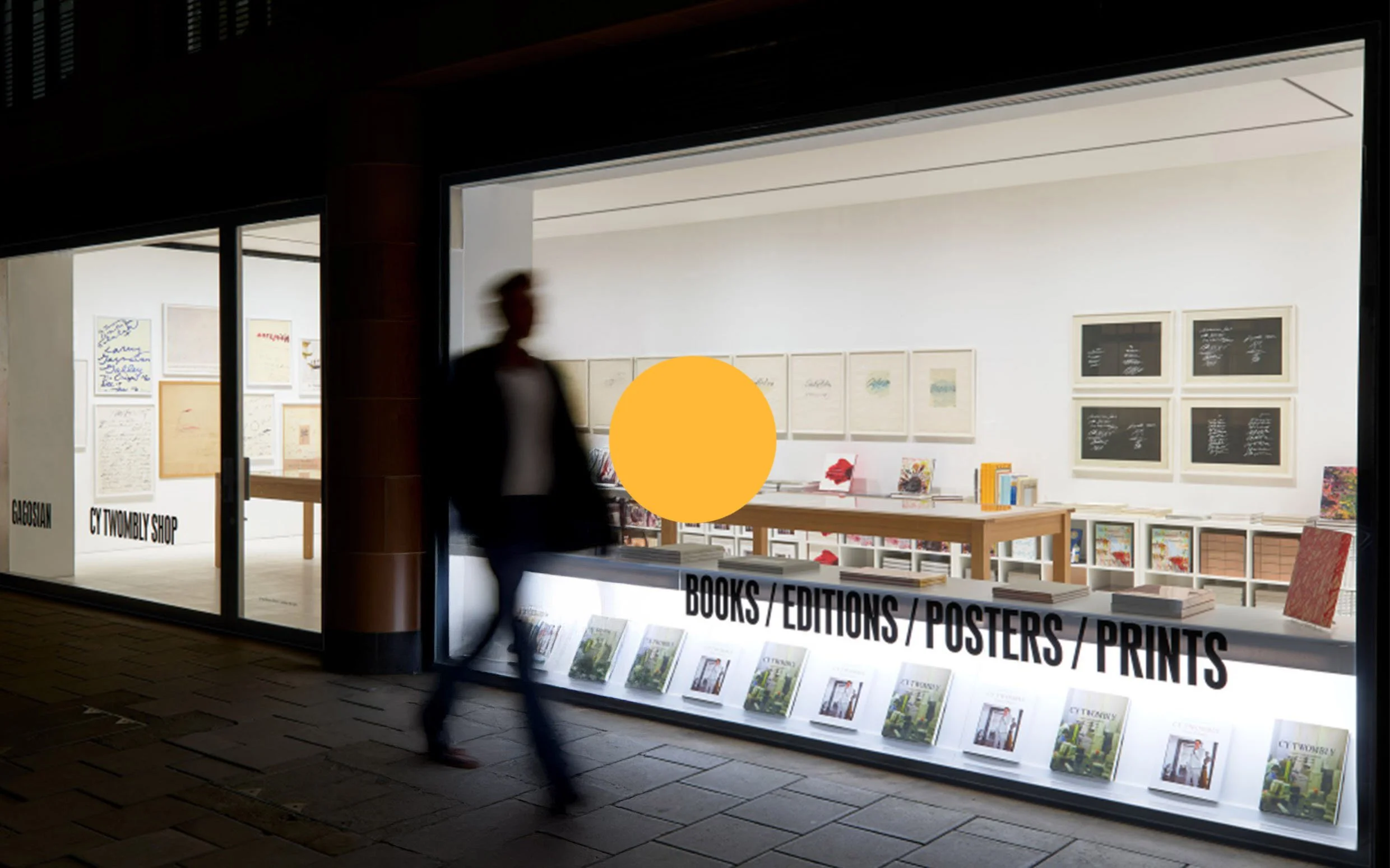 A blurred person walking past a bookstore window display with books, posters, and prints, and a sign indicating the shop sells books, editions, posters, and prints.