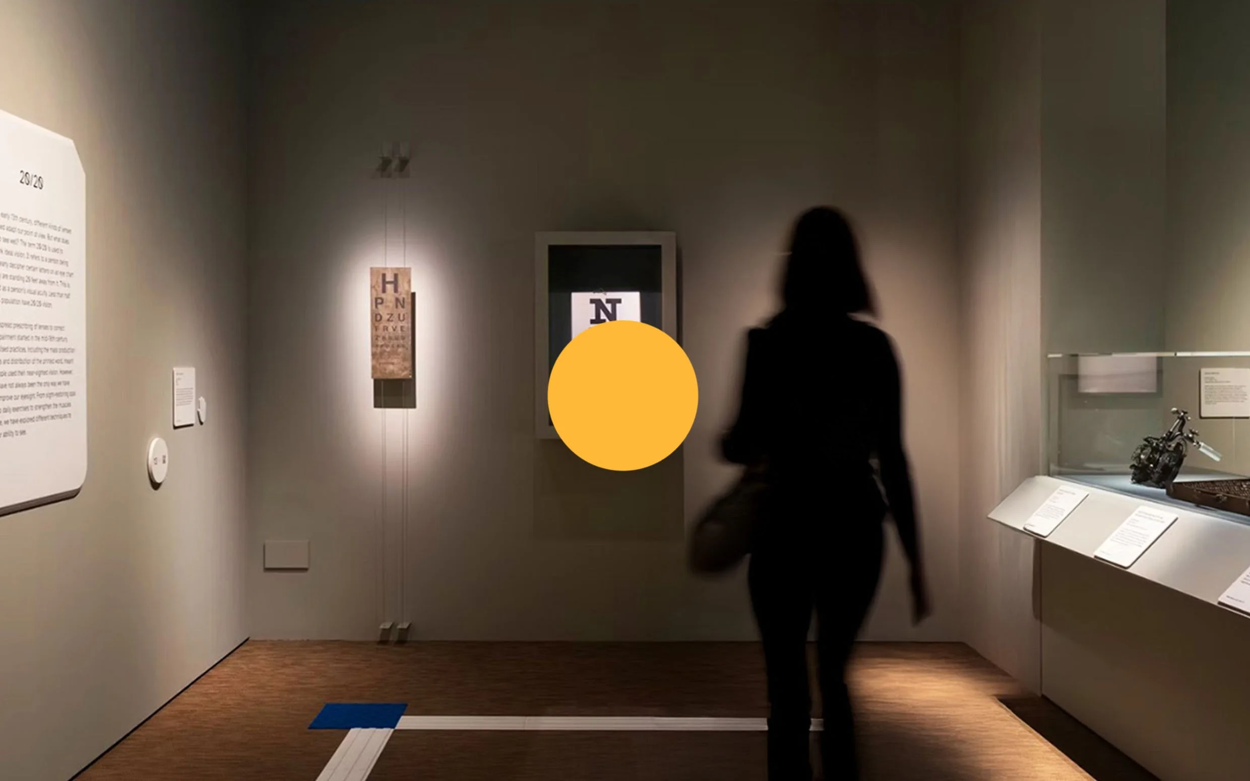 A woman walking through an art museum gallery, viewing displayed artwork and text panels.