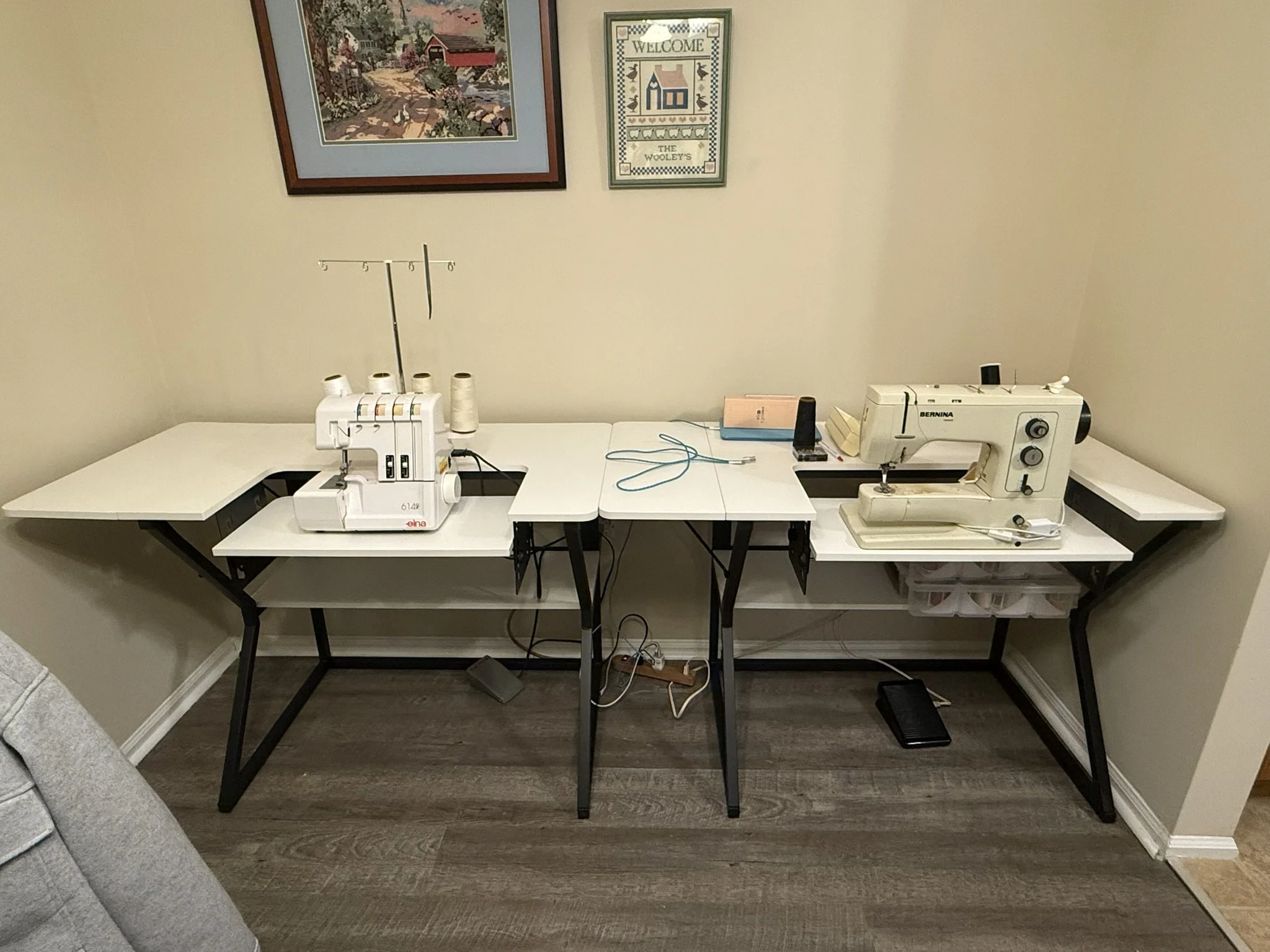A sewing room corner with two sewing machines, spools of thread, a needle, and sewing accessories on a U-shaped table.