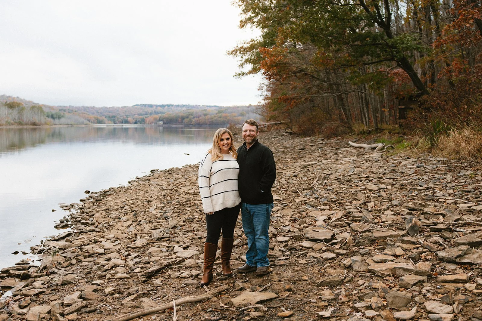 Engaged Couple standing on a beach at Quemahoning Dam smiling for a photo.