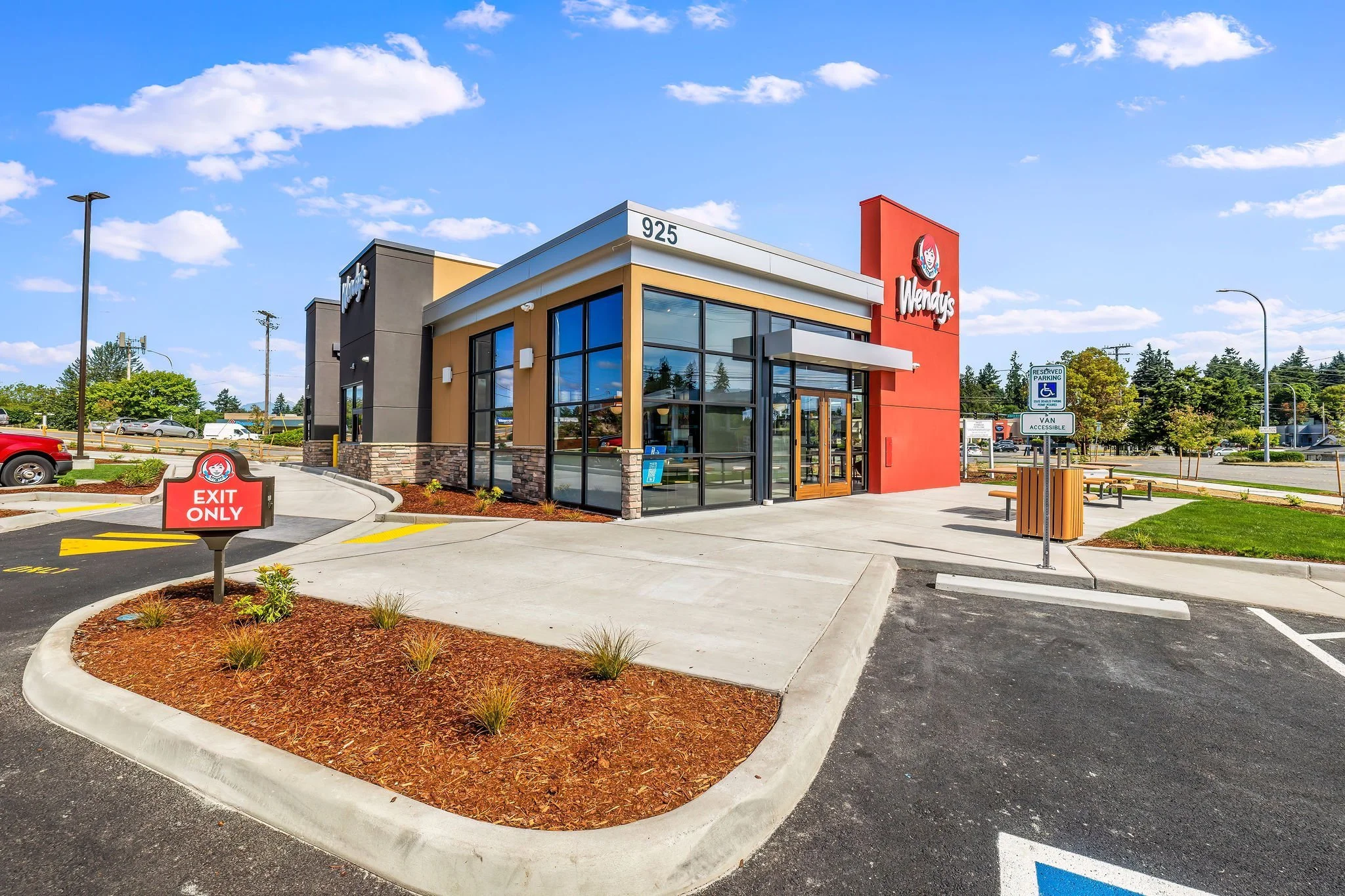 Exterior of a Wendy's fast-food restaurant with a modern glass and brick design, parking lot, and clear blue sky.