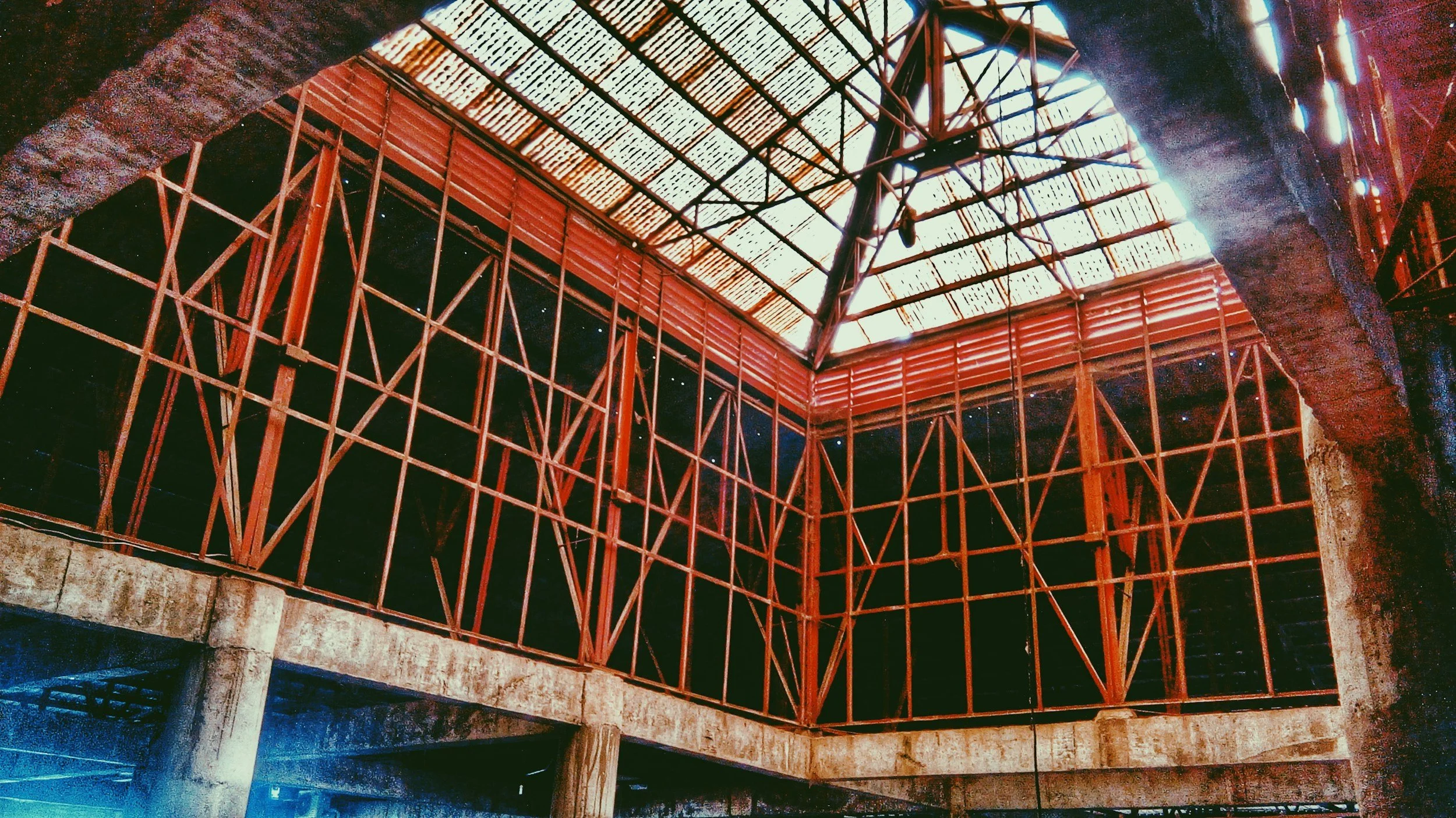 Interior of a building under construction with visible metal framing and a partially finished roof, concrete columns, and dark openings.