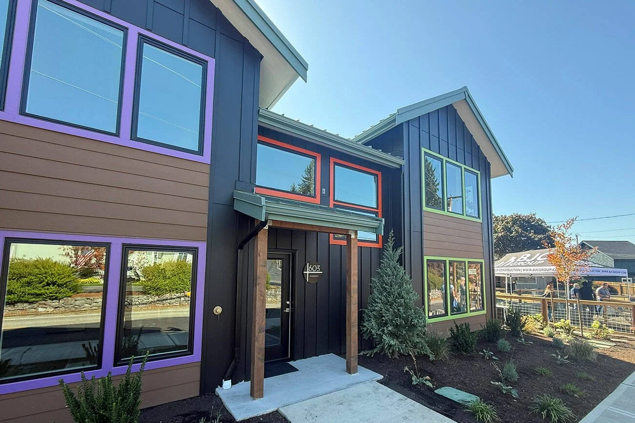 Exterior of a modern two-story residential building with colorful window frames, black and brown siding, and newly landscaped garden.