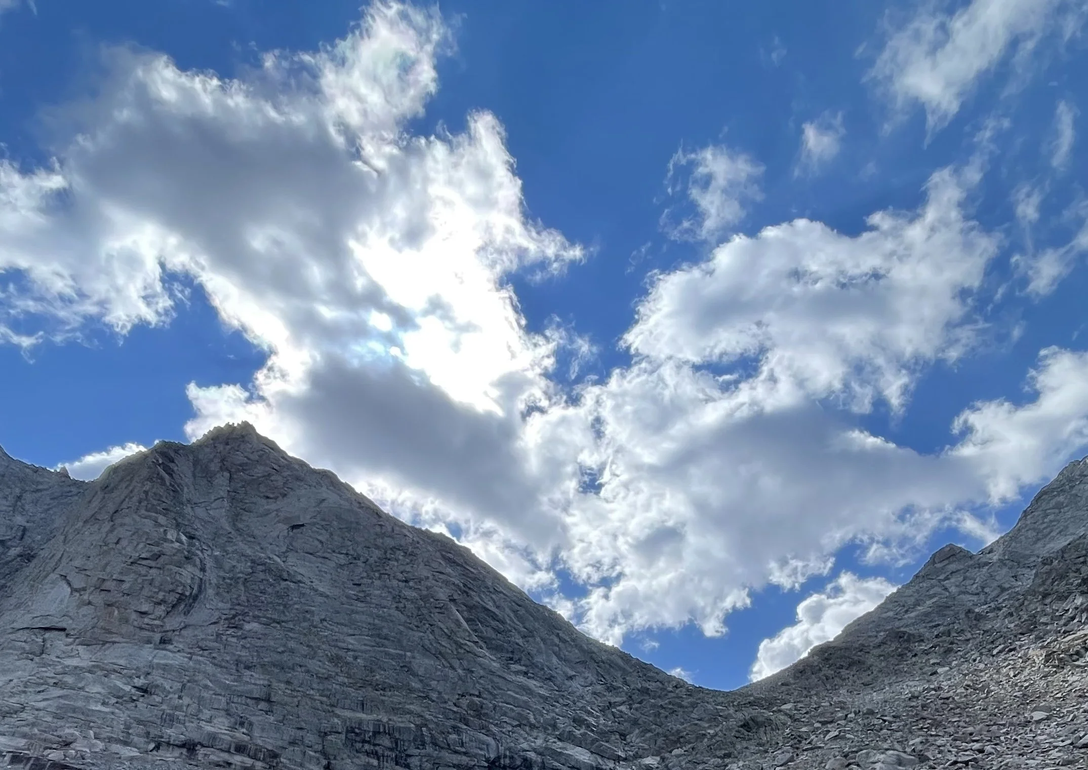 View of rocky mountain peaks under a blue sky with scattered white clouds.