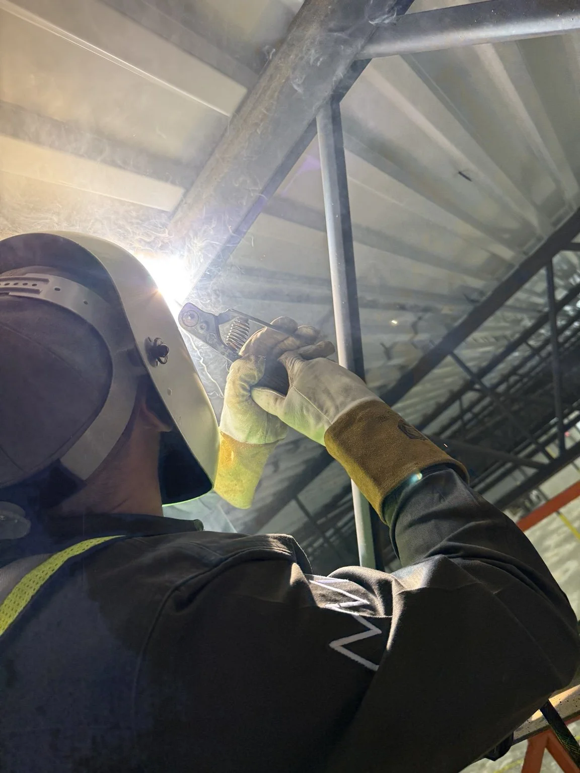 Welder working overhead on a metal roof beam.