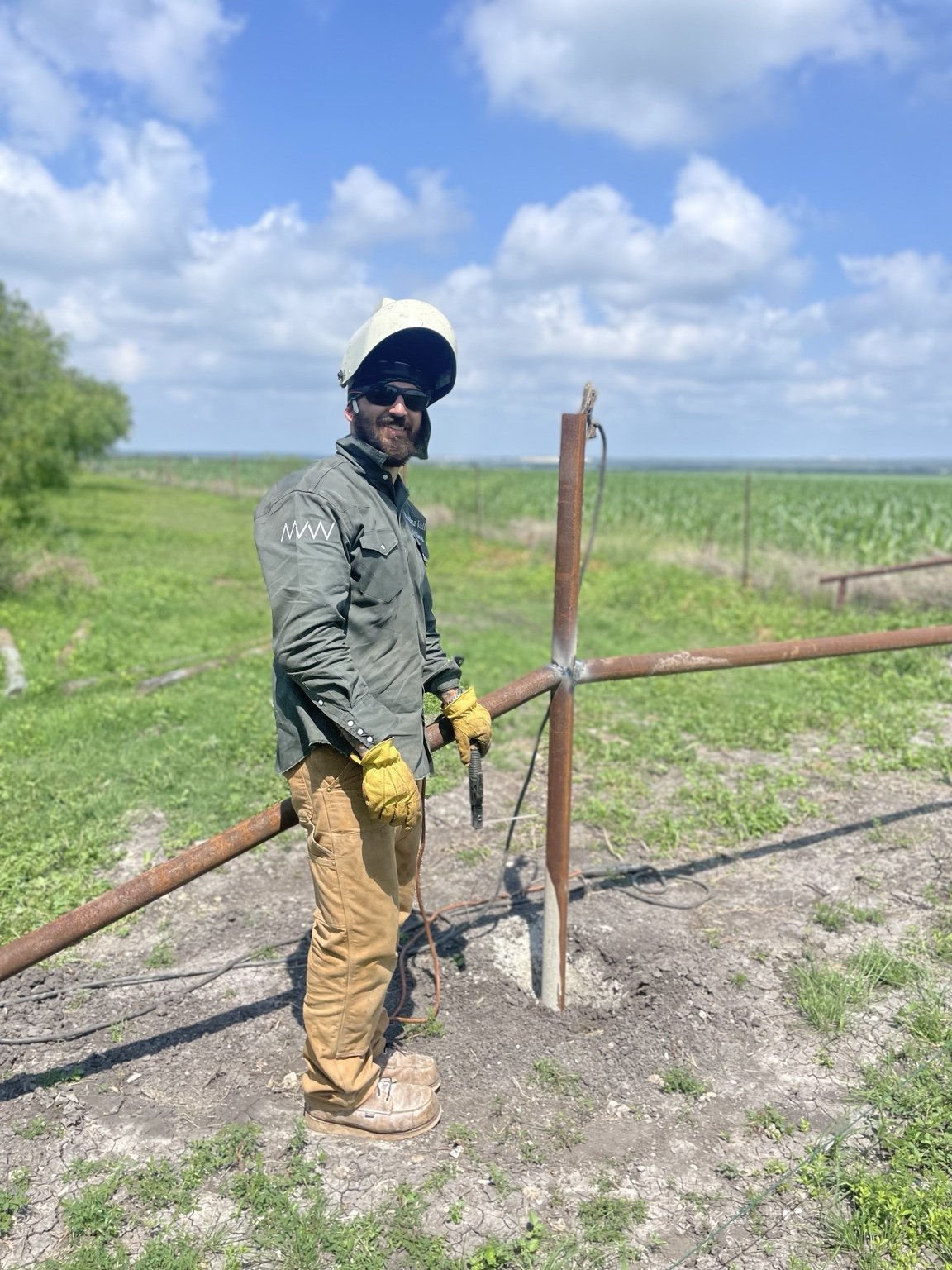 Welder in work gear beside a pipe fence under construction.