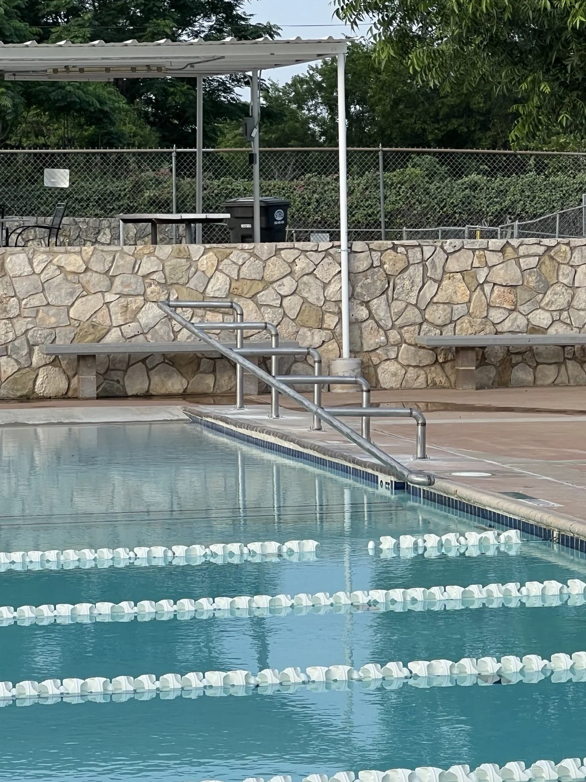 Long metal handrail with multiple supports installed along a swimming pool edge.
