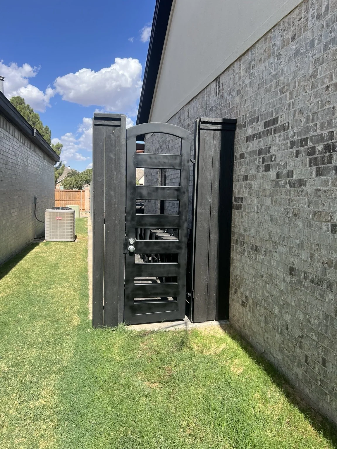 Custom black metal pedestrian gate with an arched top beside a brick wall.