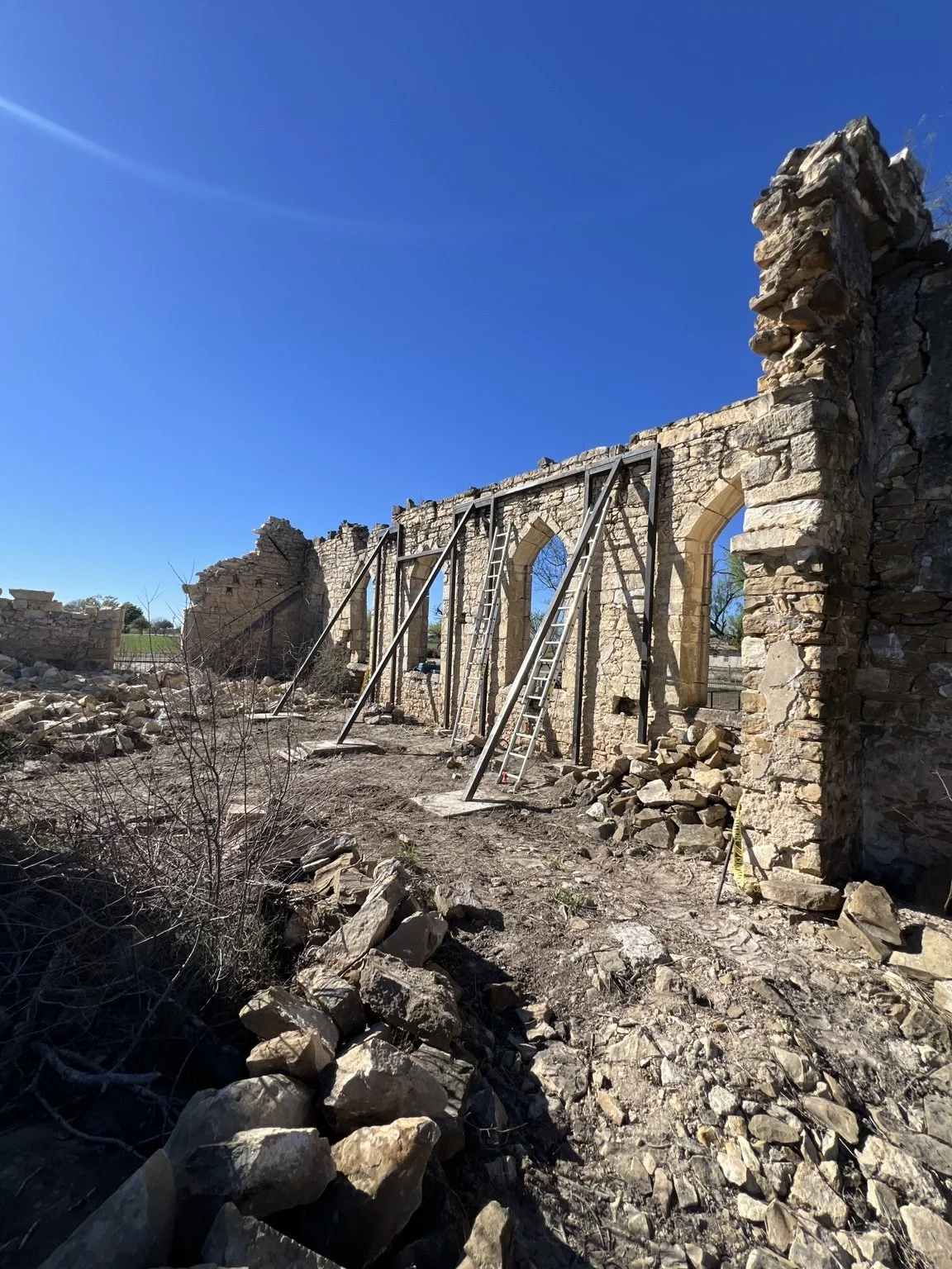 Diagonal metal braces supporting a standing stone wall with arched openings.