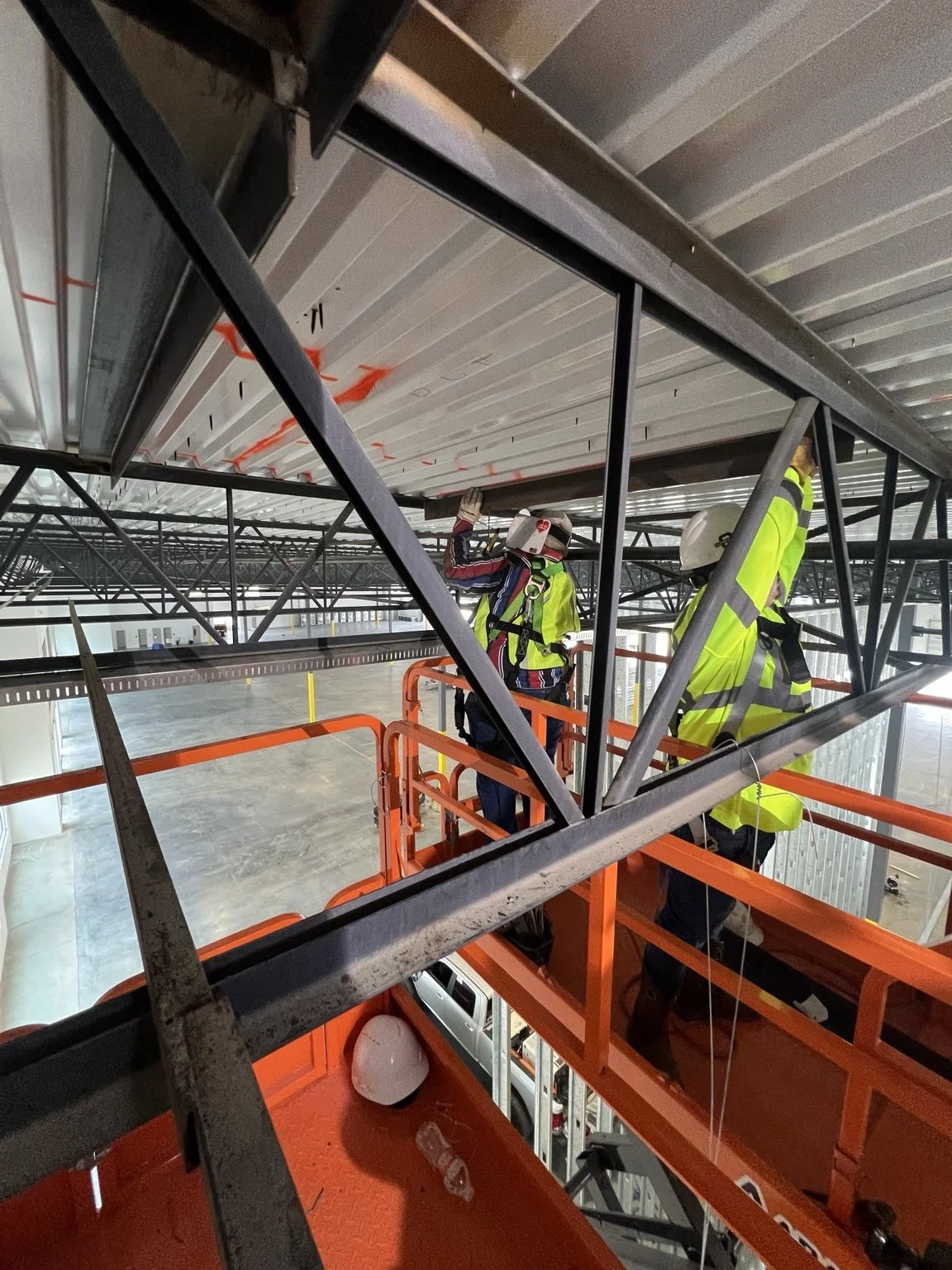 Workers on a lift welding overhead metal framing inside a commercial building.