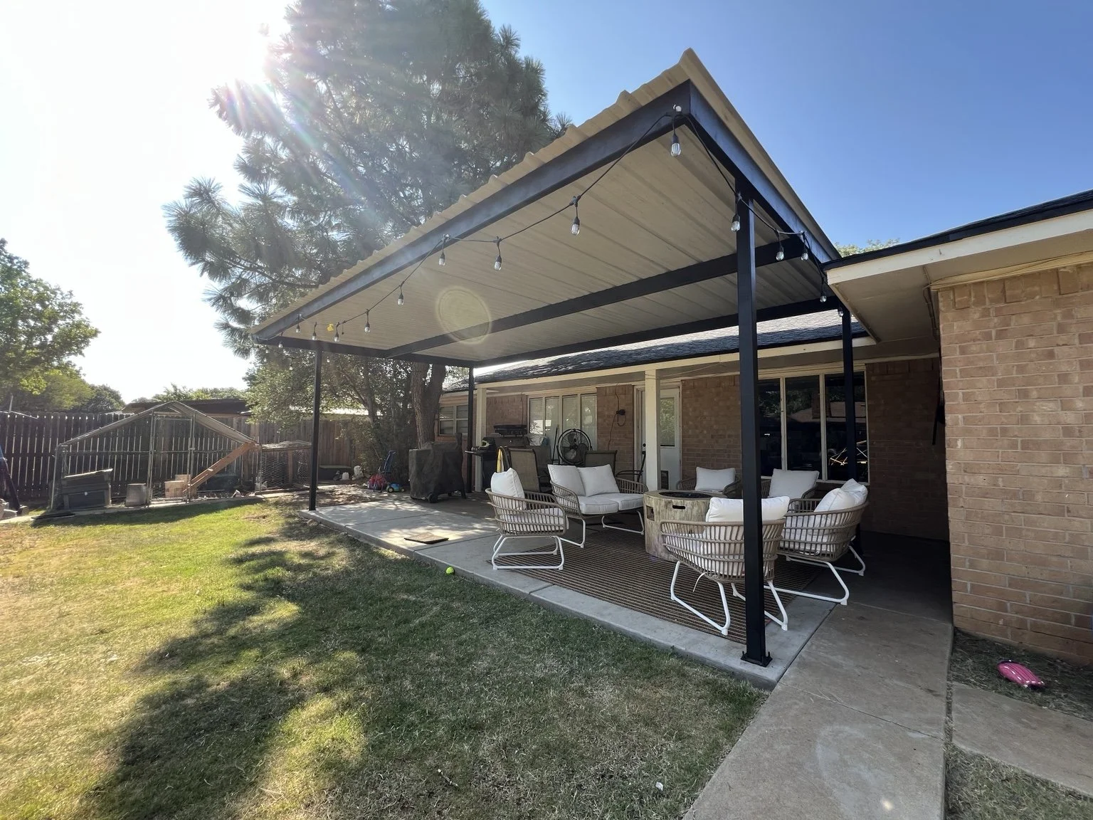 Black metal patio cover with light roof panels over a furnished backyard patio.