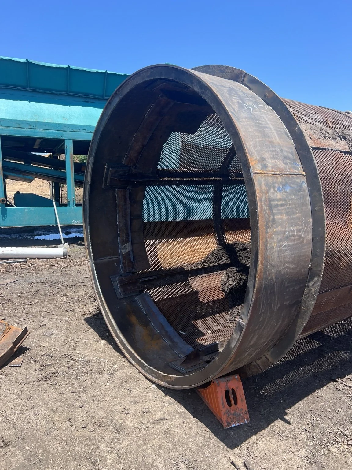Large cylindrical screening drum with welded curved plates and internal metal bracing.