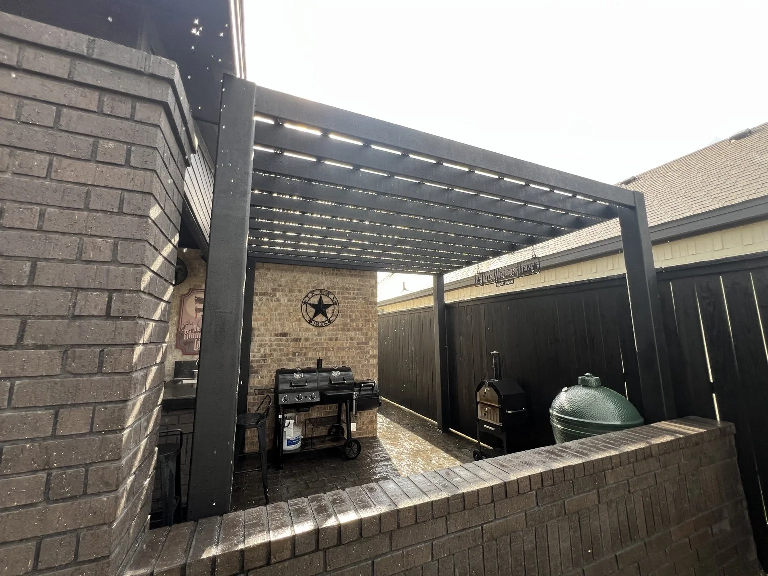 Black metal pergola over an outdoor kitchen and grilling area.