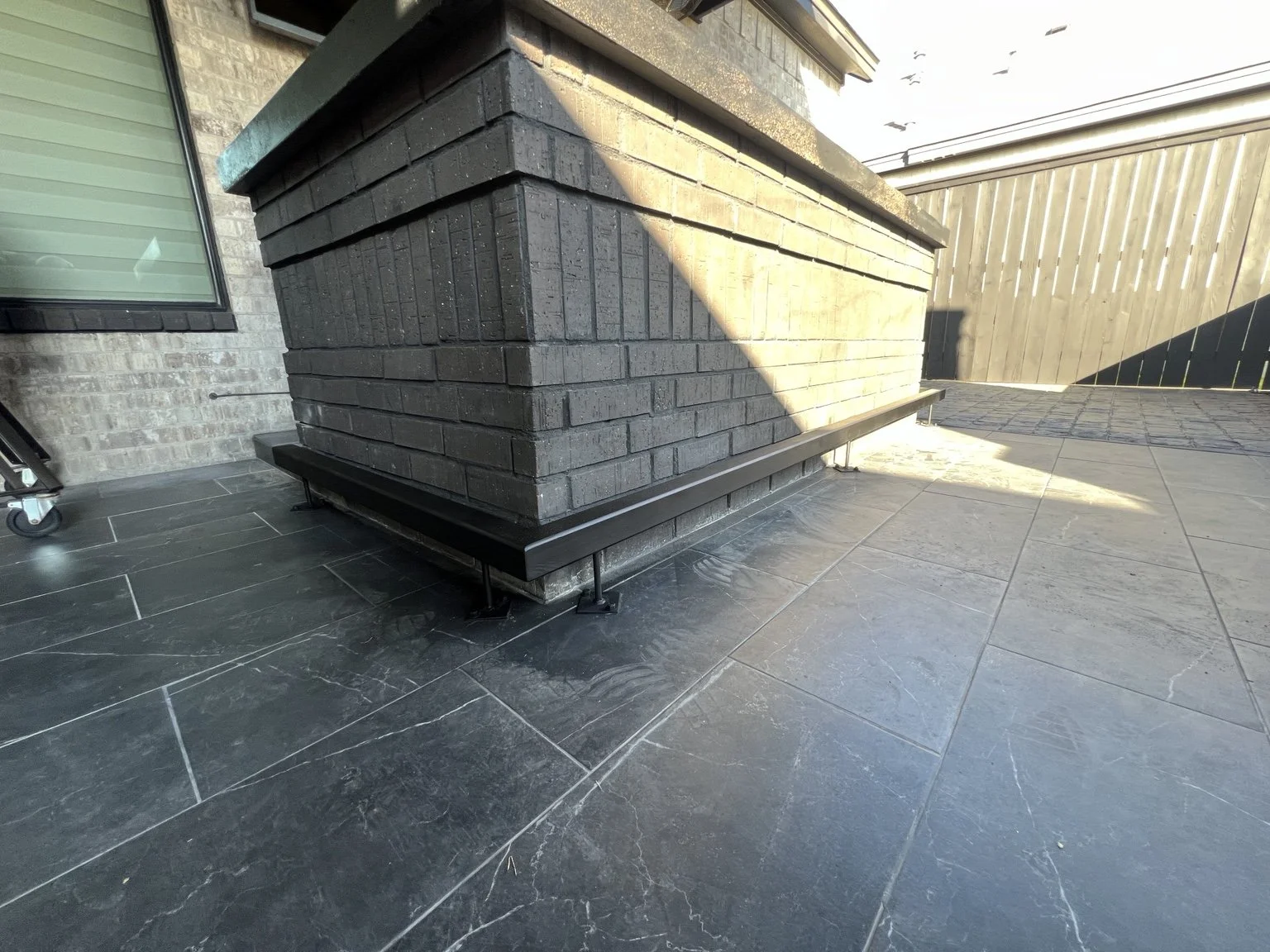 Black metal foot rail fitted around an outdoor brick bar.