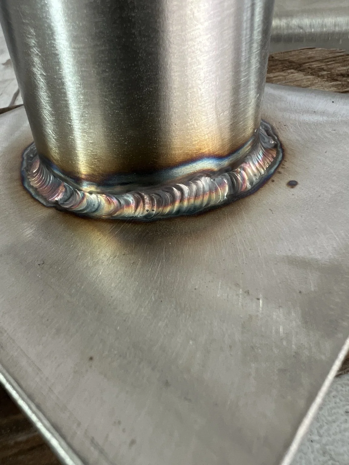 Close view of a circular weld joining a round metal tube to a flat plate.
