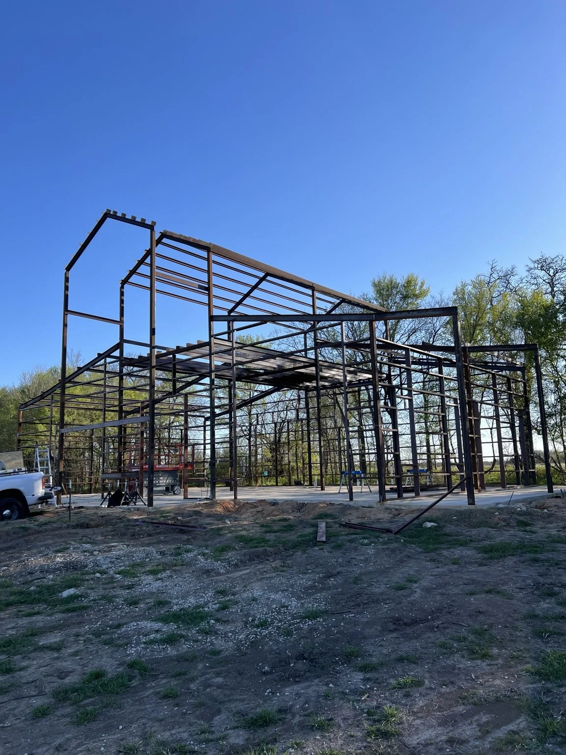 Multi-level metal building frame with roof members and an elevated floor under construction.