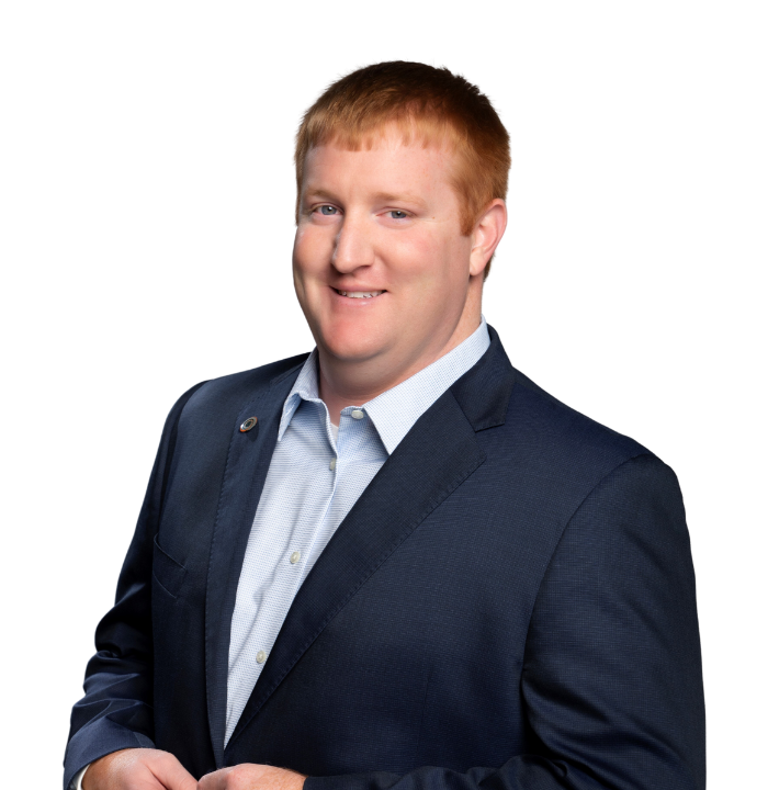 A young man with red hair in a navy blue blazer and light blue shirt, smiling in a professional portrait against a white background.