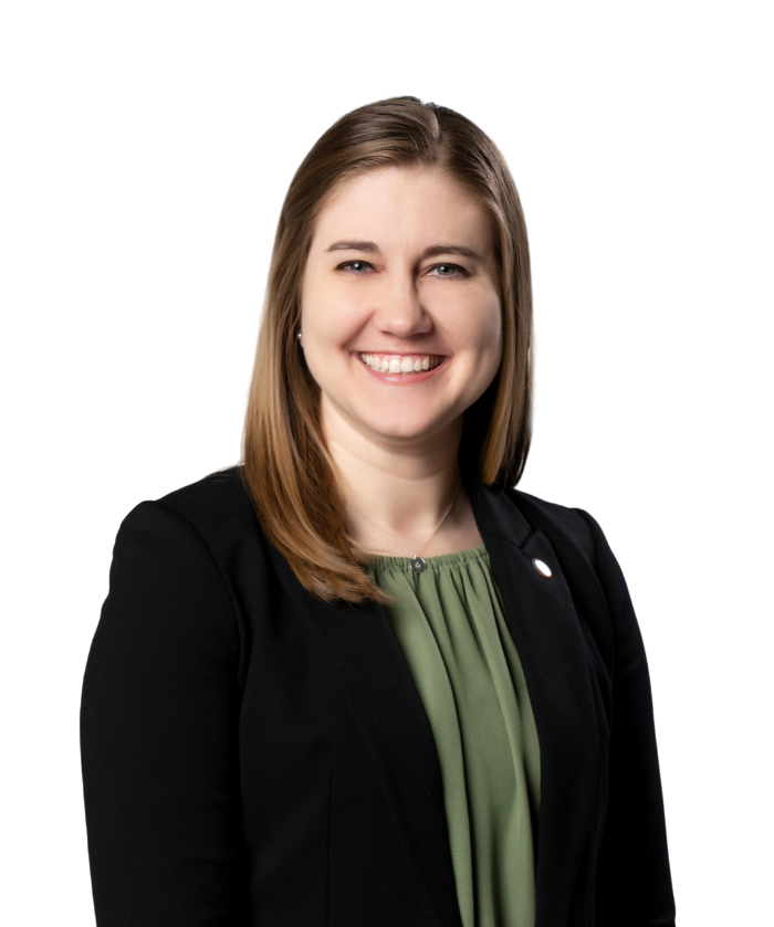 A woman with shoulder-length brown hair smiling, wearing a black blazer over a green blouse, against a white background.