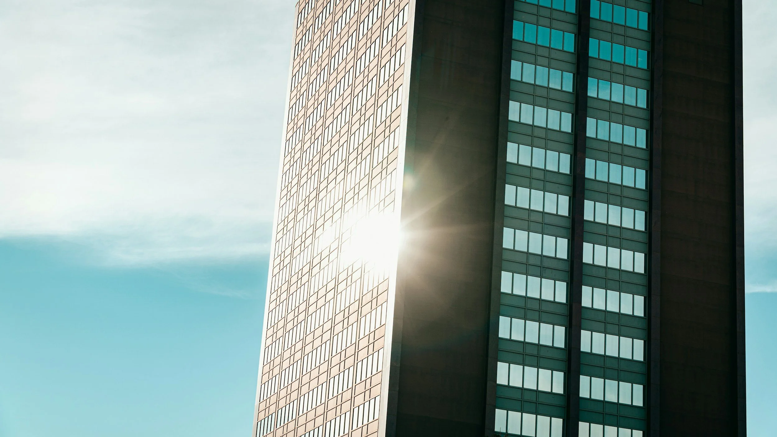 Sunlight reflecting off the glass windows of a tall, modern building against a blue sky with some clouds.