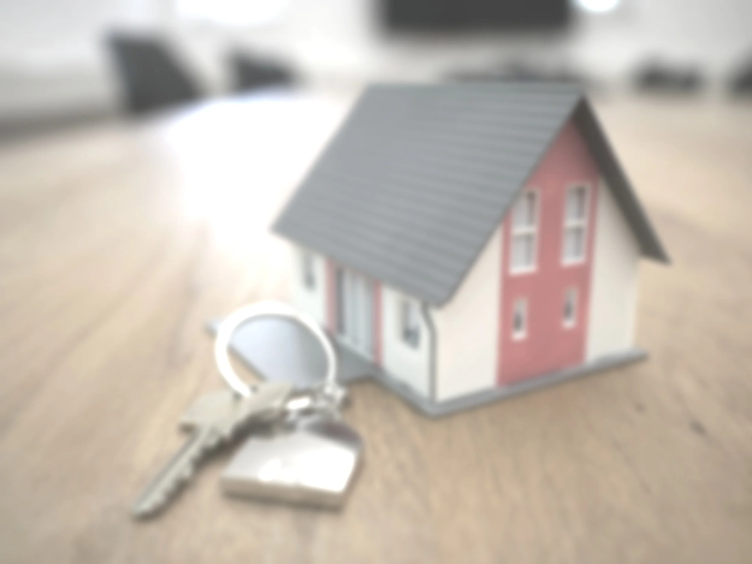 A small model house with a gray roof and pink and white walls, along with a set of keys, on a wooden surface.