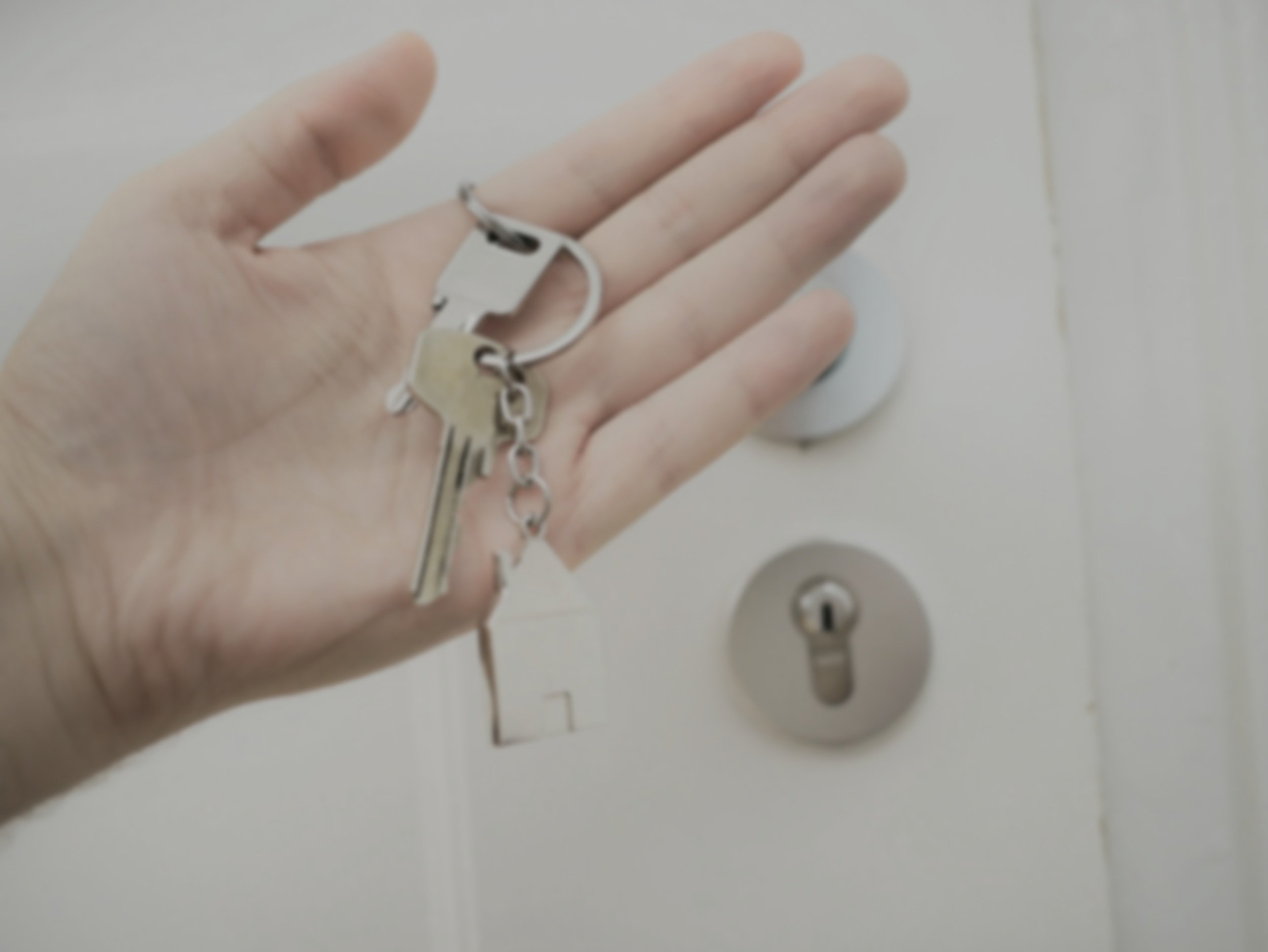 A person's hand holding a keychain with two keys in front of a white door lock.