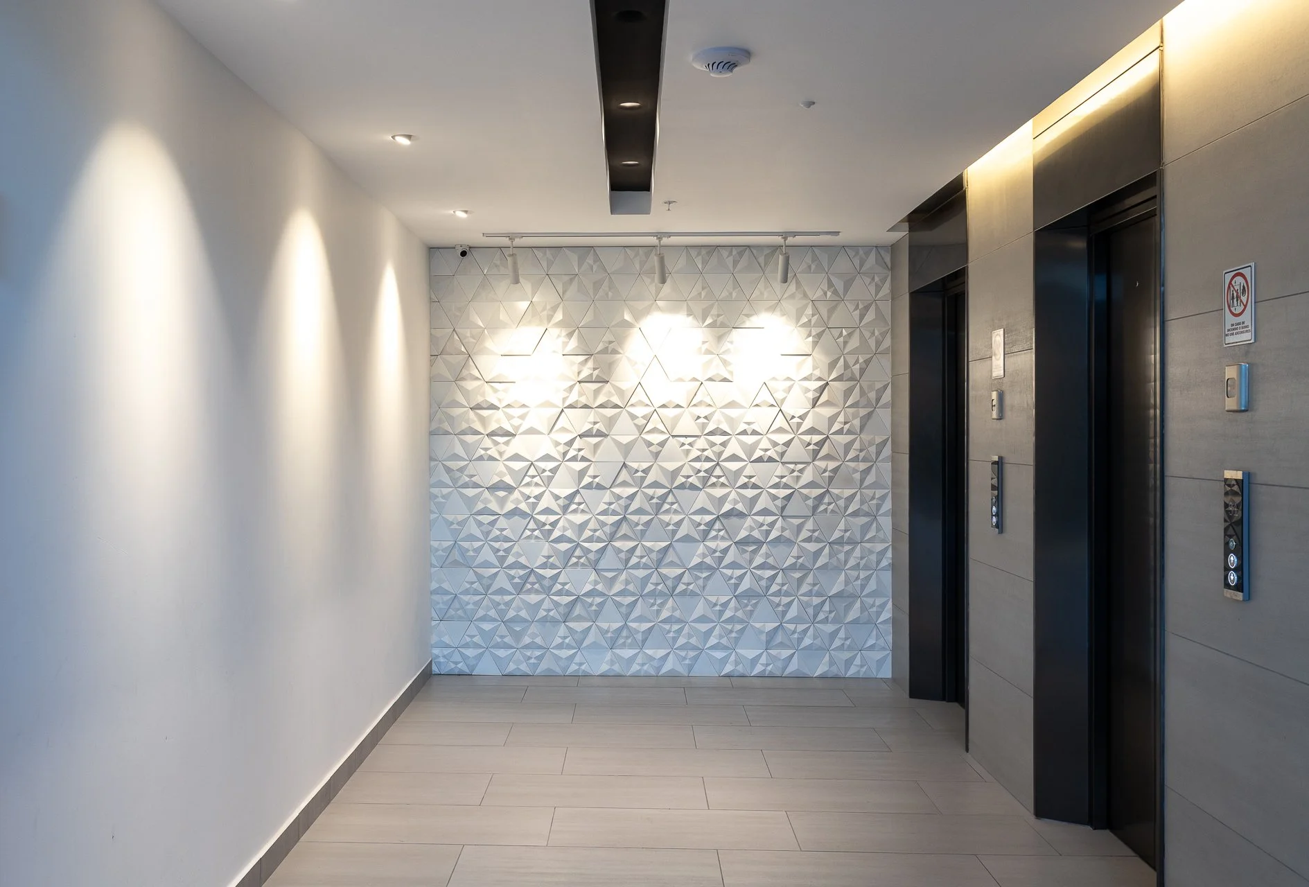 Ascensor en un vestíbulo con paredes blancas y una pared decorativa en relieve