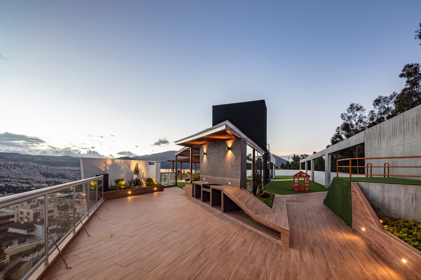 Terraza moderna en la azotea con vista urbana y áreas verdes, con iluminación y estructura de madera.