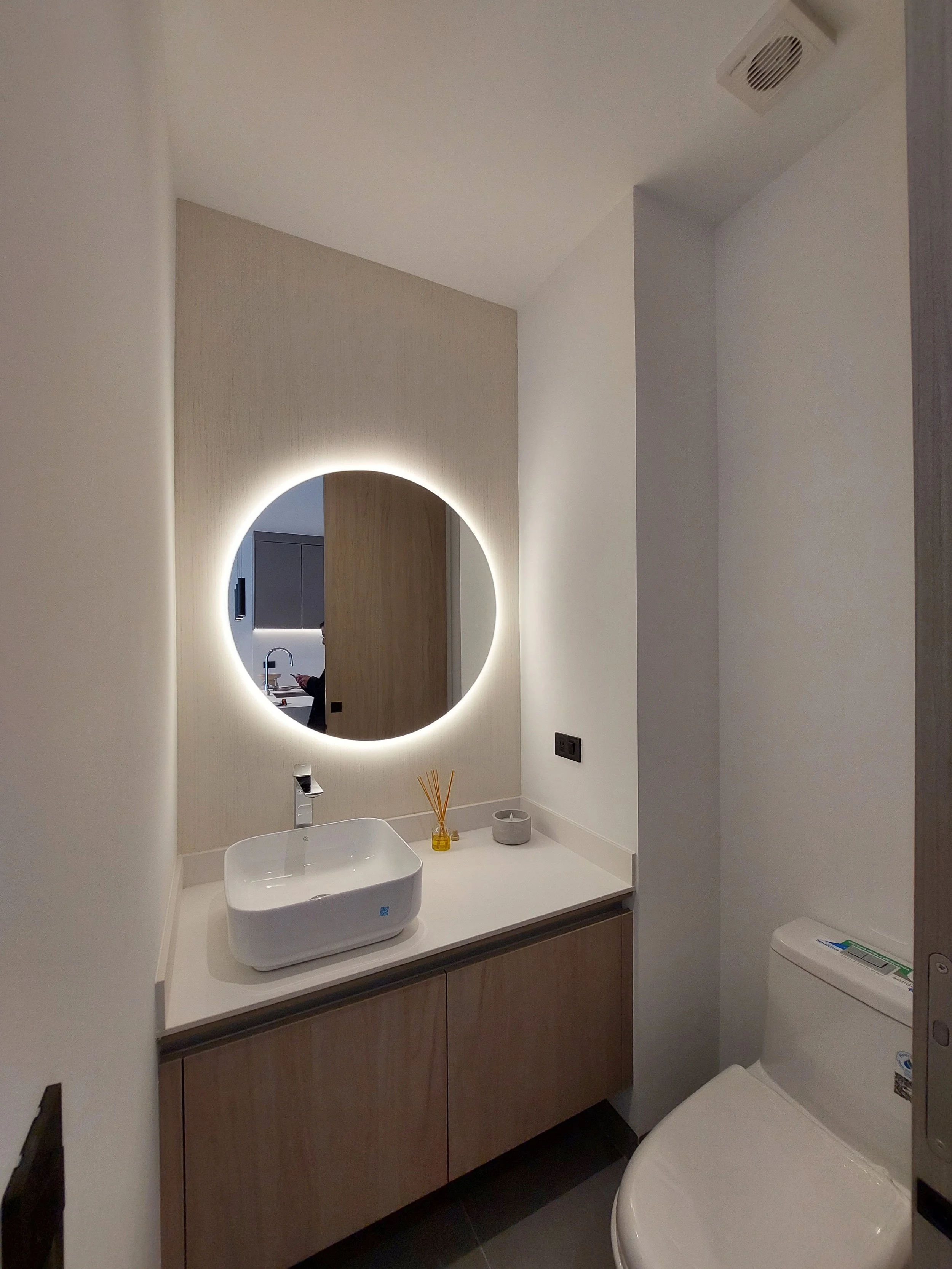 Baño moderno con lavabo rectangular, espejo con iluminación LED, inodoro y accesorios decorativos en la repisa.
