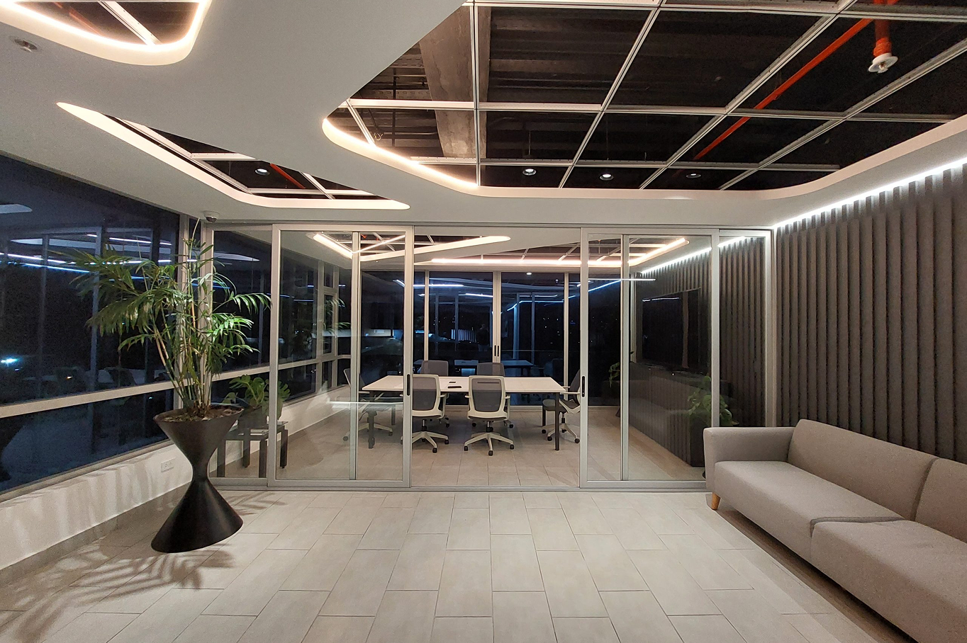 Sala de conferencias moderna con sillones y mesa en una oficina, con ventanas de vidrio y iluminación LED, durante la noche.