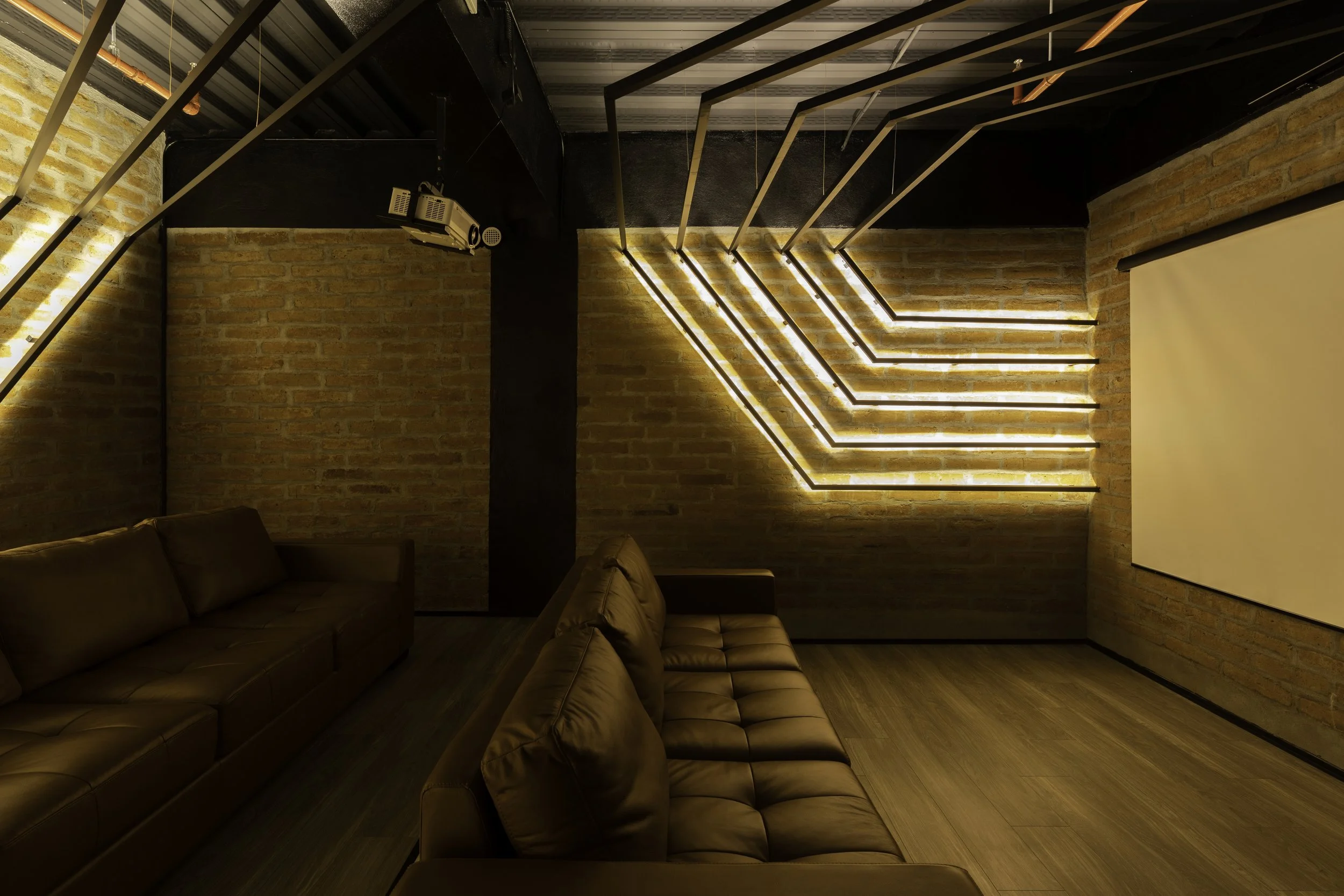 Sala de cine moderna con paredes de ladrillo, sillones de cuero marrón, y luces led en forma de zigzag en la pared.