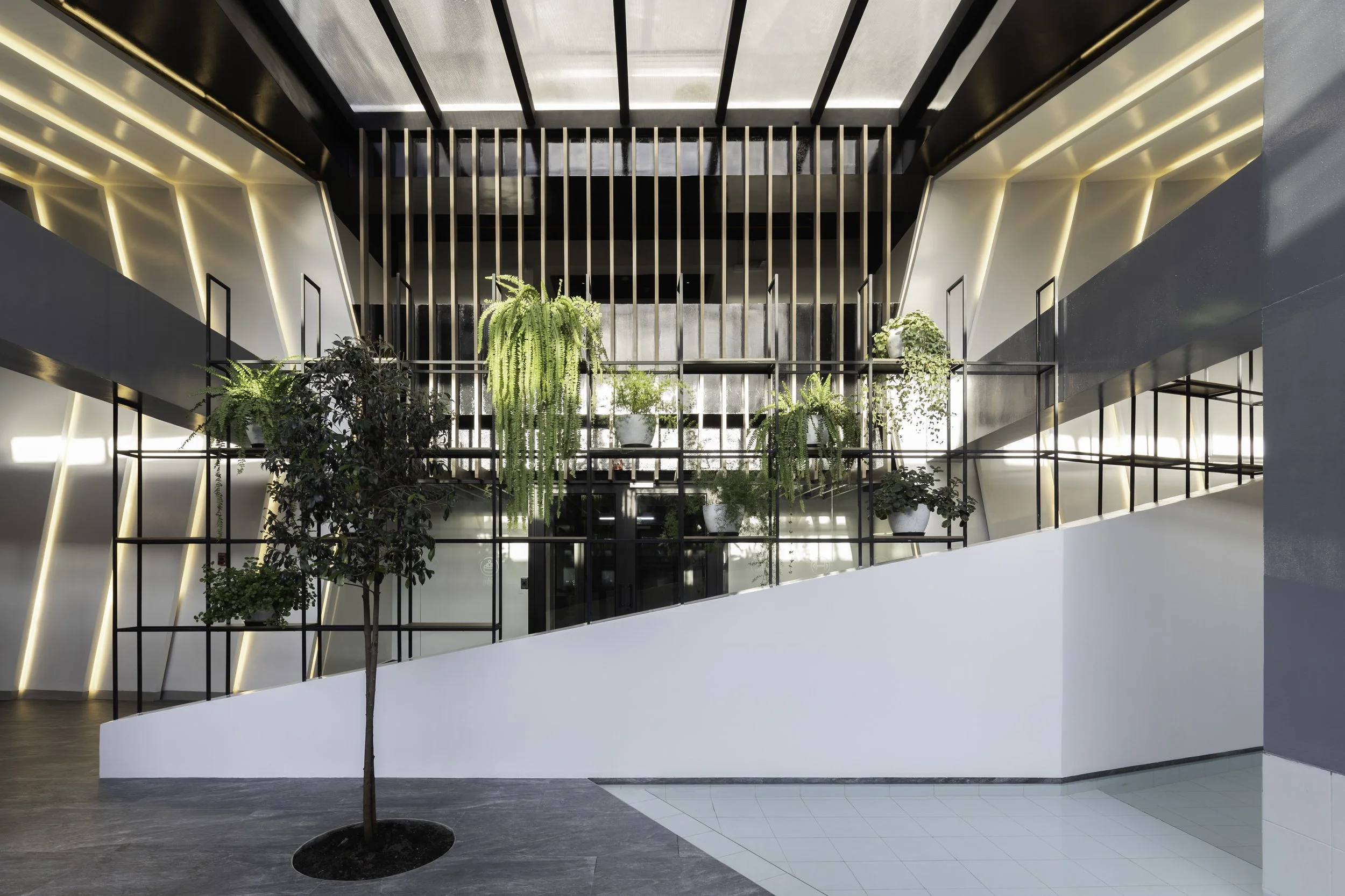 Interior moderno de un edificio con plantas en macetas blancas en una estructura de metal negro y paredes con iluminación LED, con escaleras blancas.