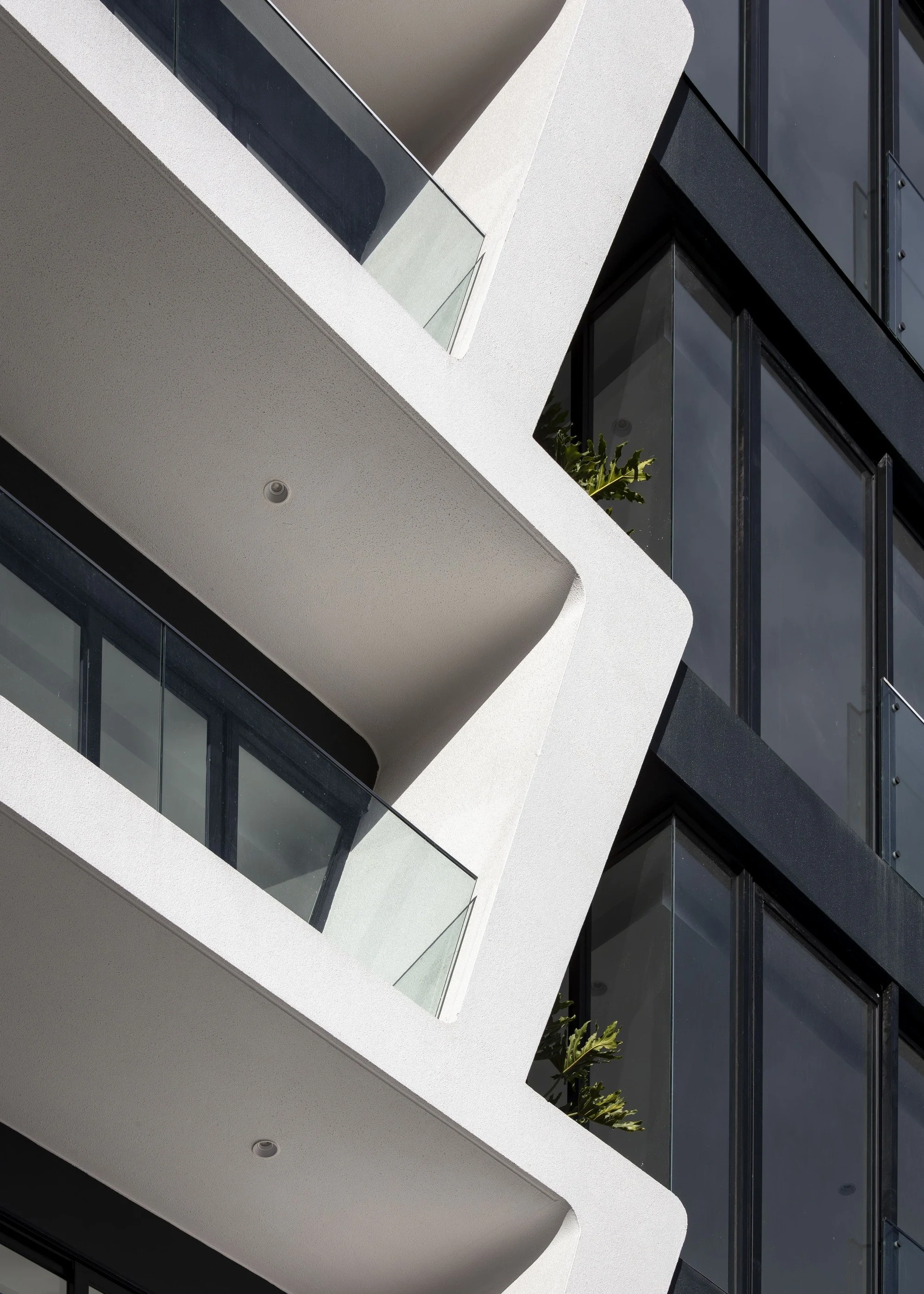 Fachada moderna de edificio con balcones blancos y ventanas de vidrio oscuro.