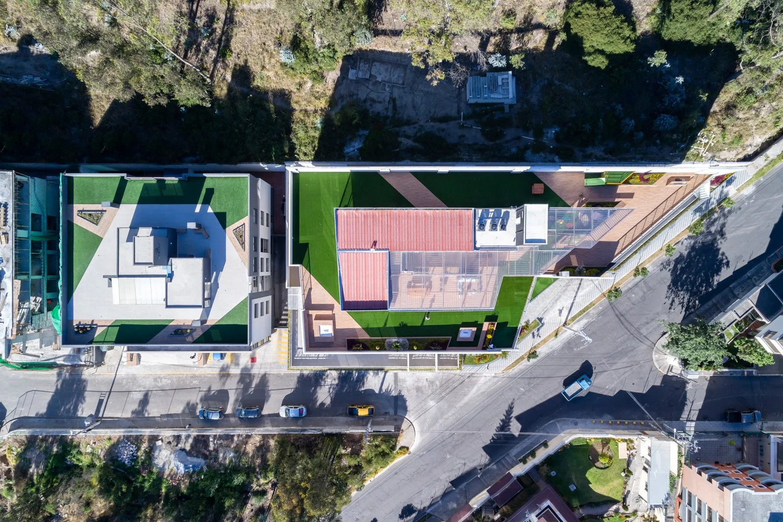 Vista aérea de dos edificios con azoteas verdes, separados por una calle en una zona urbana con árboles y edificios cercanos.
