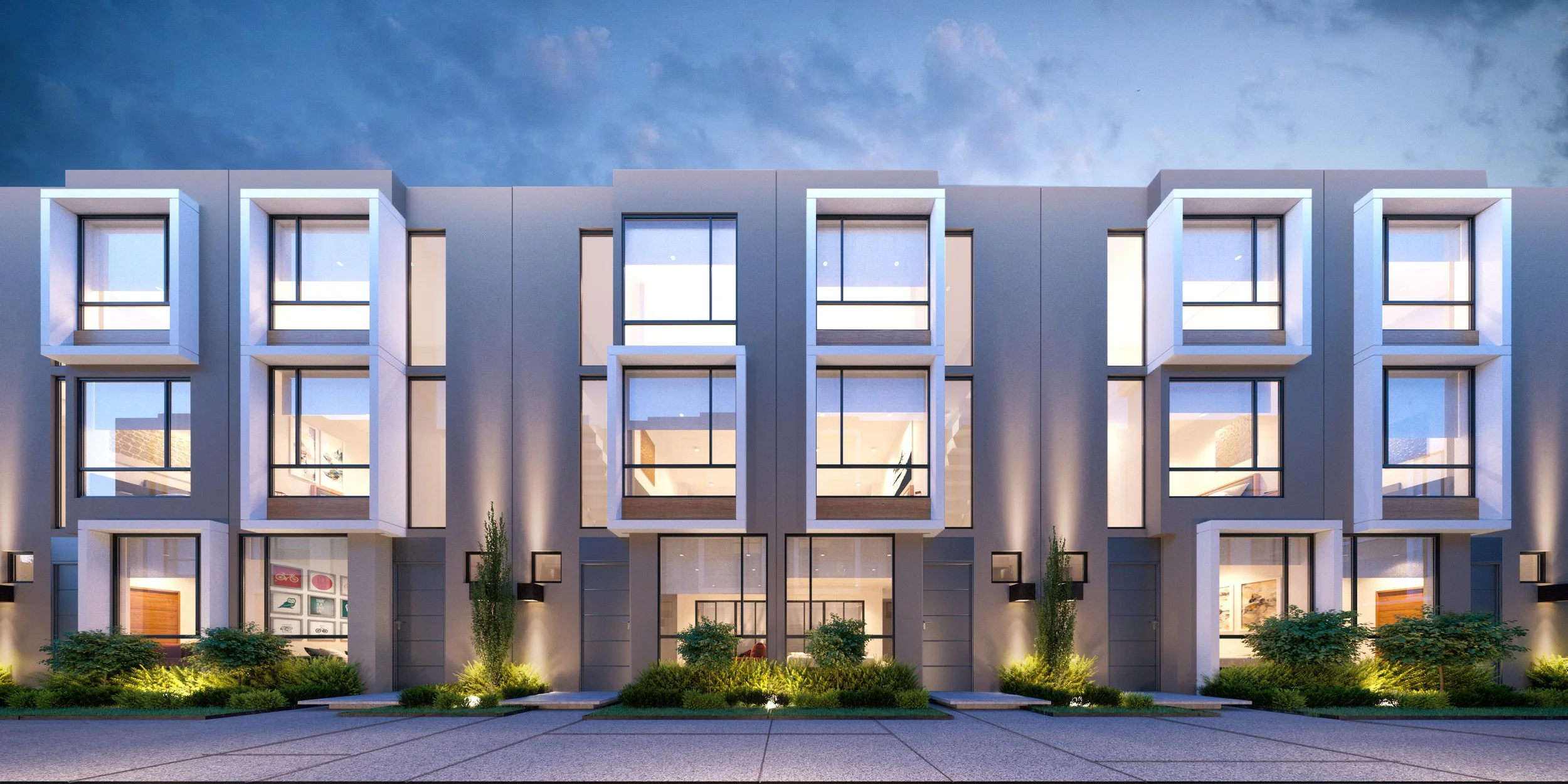 Edificio moderno de varias plantas con ventanas grandes y iluminación exterior, rodeado de áreas verdes y un camino pavimentado.