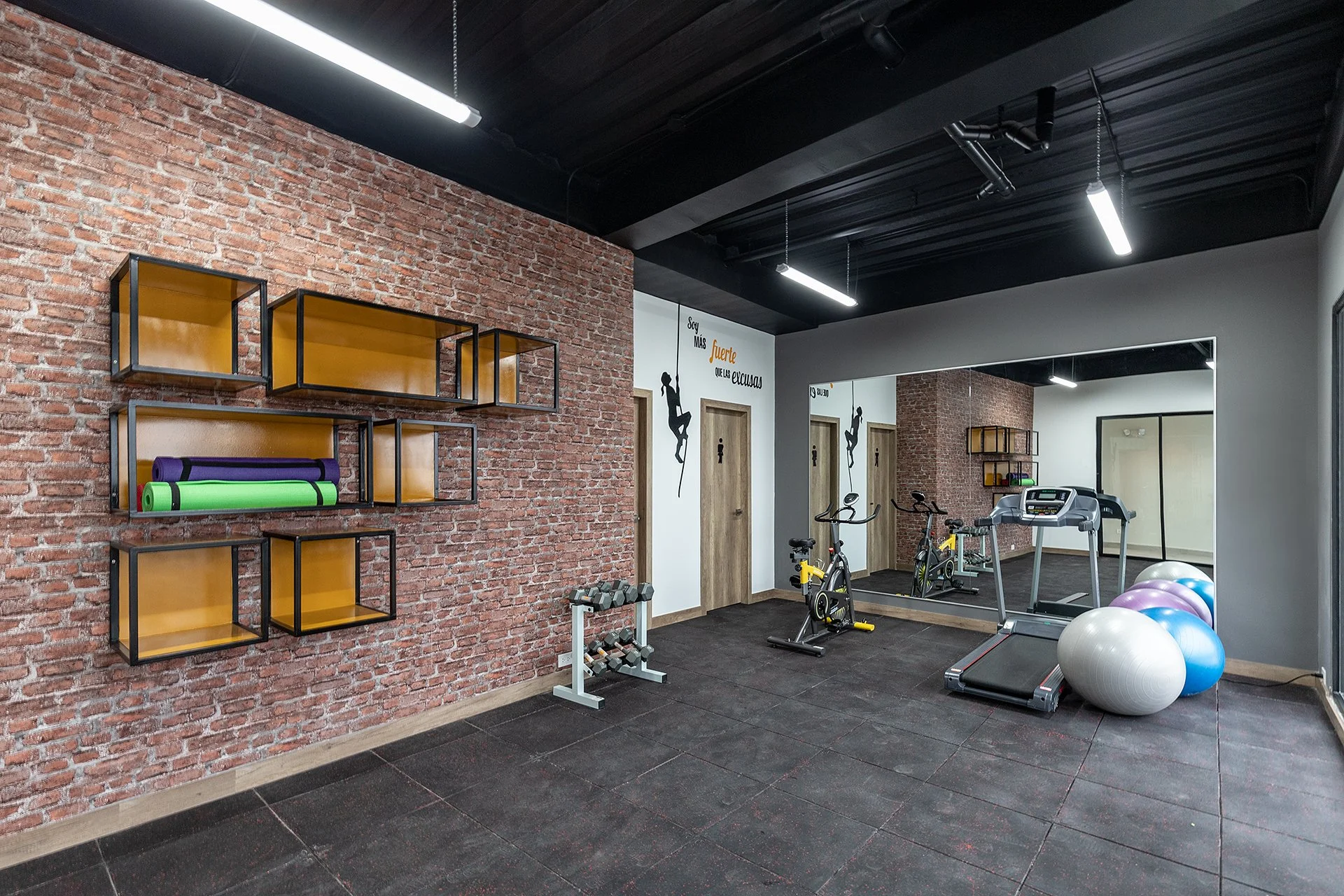 Gimnasio con pared de ladrillos, equipo de ejercicio, balones de baloncesto y un espejo grande