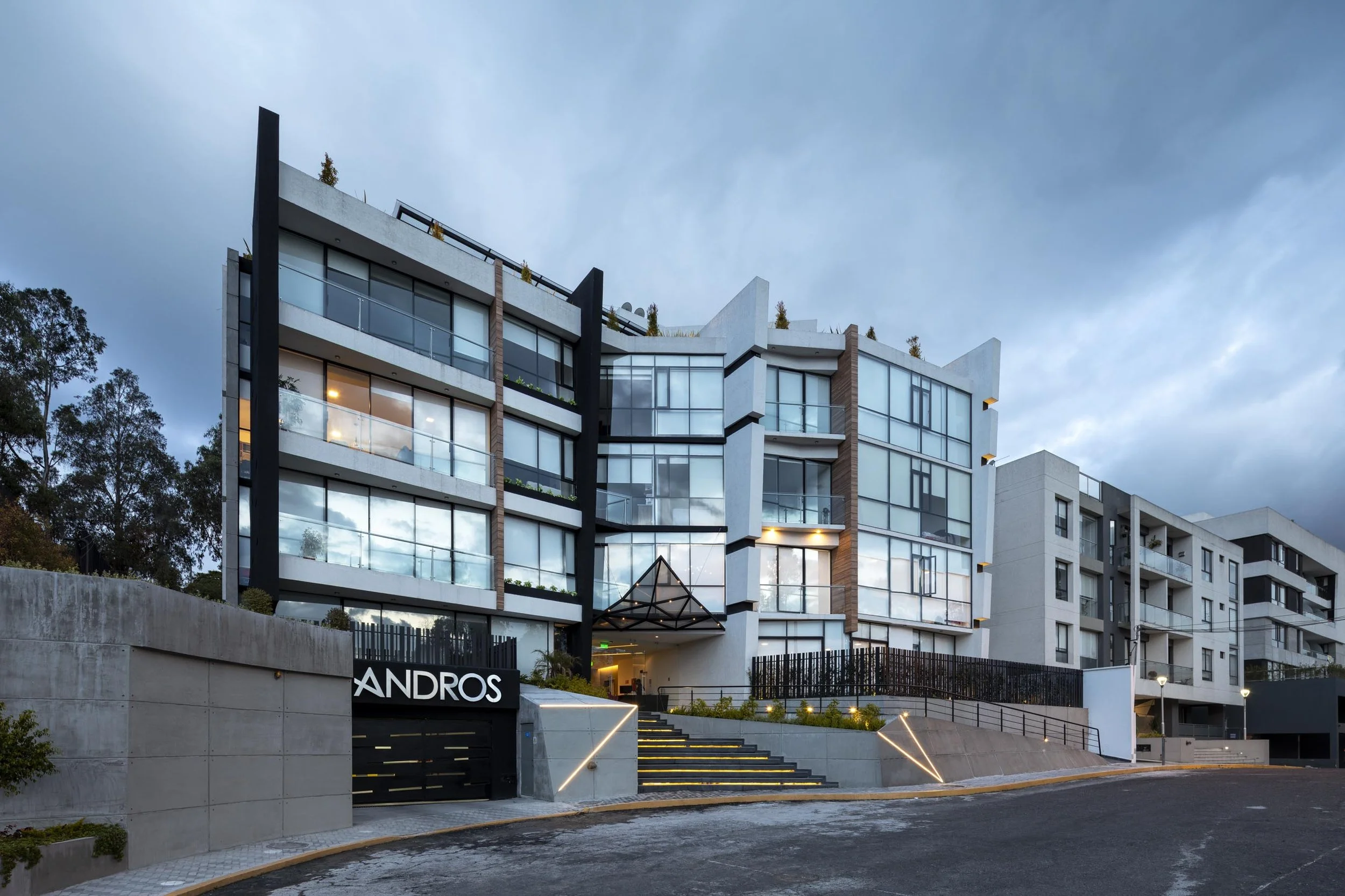 Edificio moderno de varios pisos con fachada de vidrio y luces en las escaleras exteriores, con el letrero 'ANDROS' en la entrada.
