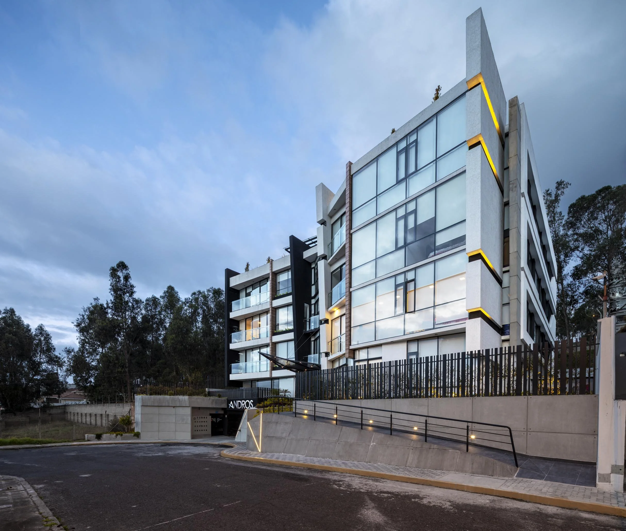 Edificio moderno de varios pisos con fachadas de vidrio y luces exteriores, en condición de atardecer.