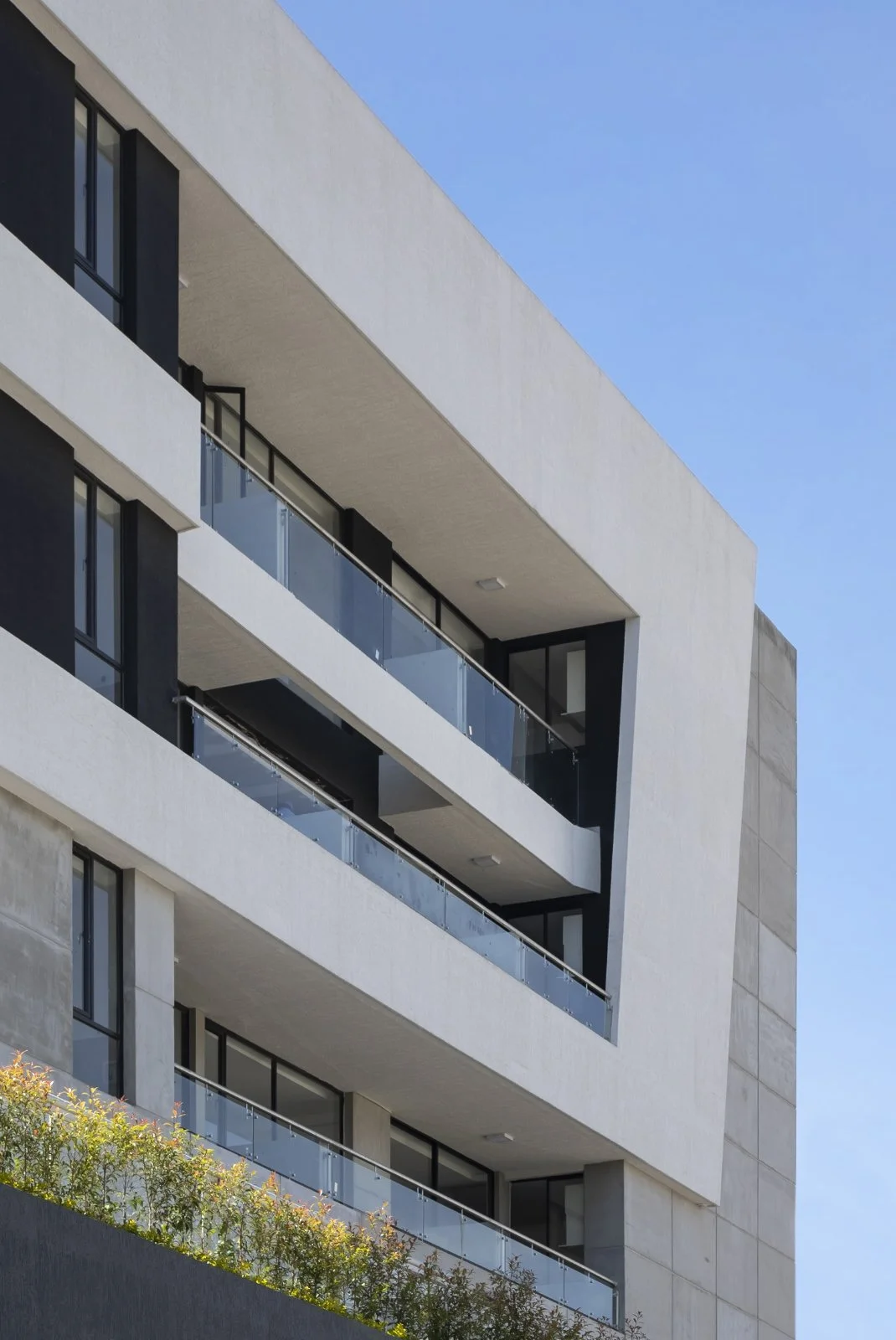 Edificio moderno con balcones de cristal y ventanas grandes, en un día soleado con cielo azul.