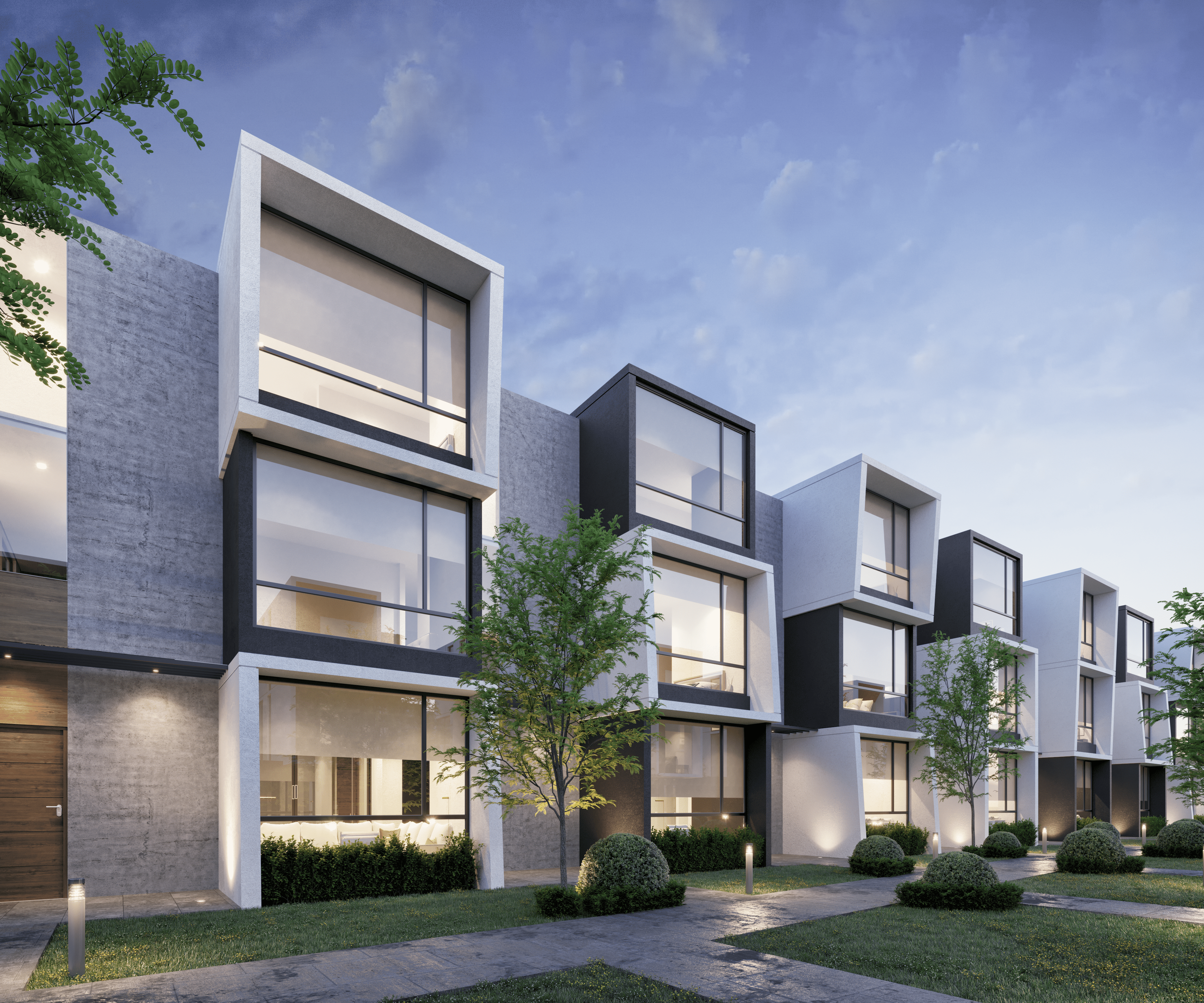 Conjunto de casas modernas de varios pisos con fachadas blancas y negras, áreas verdes con arbustos y árboles, y caminos pavimentados, en un ambiente urbano al atardecer.