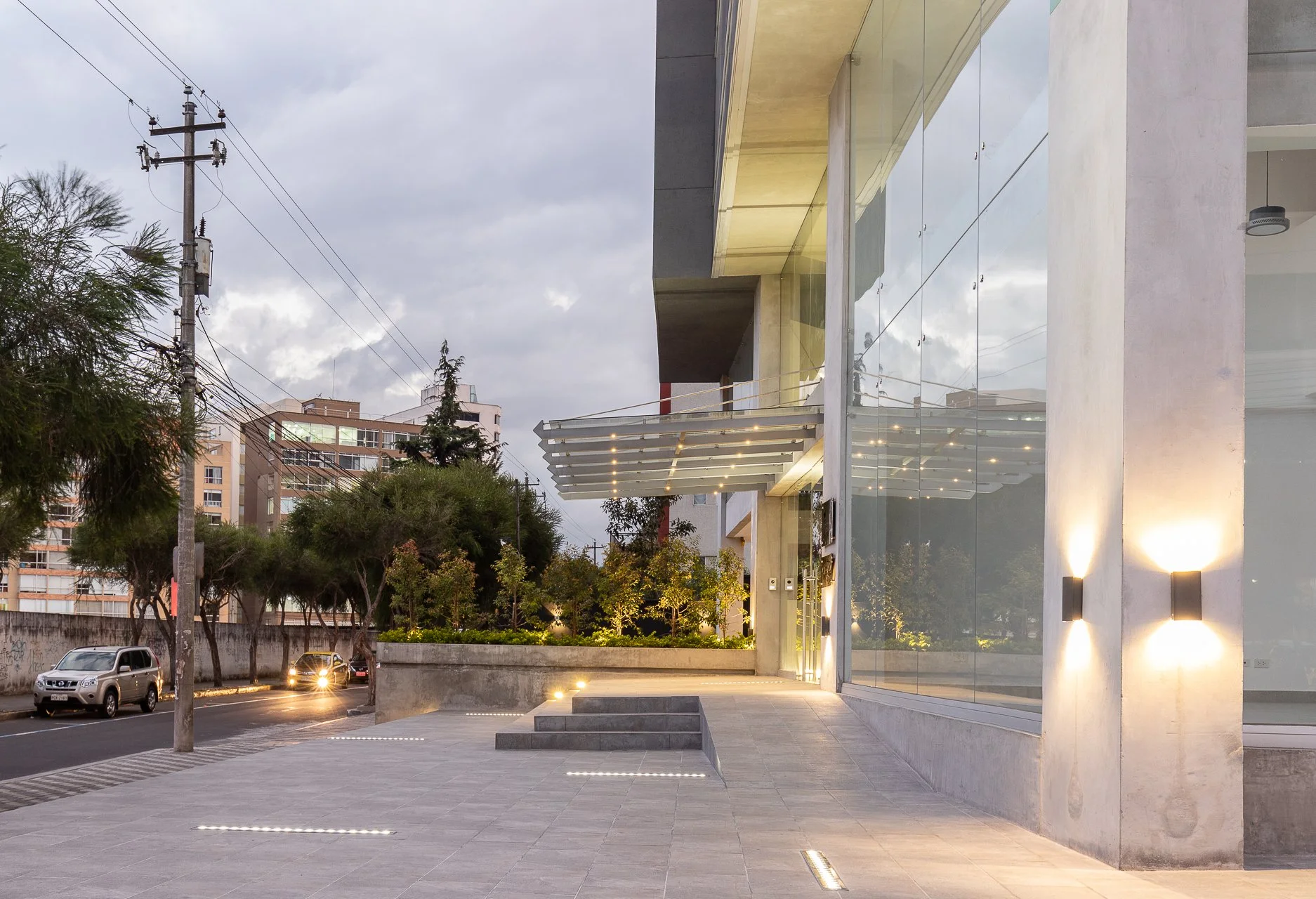 Vista de la fachada moderna de un edificio con grandes ventanales de espejo y iluminación exterior en la noche.