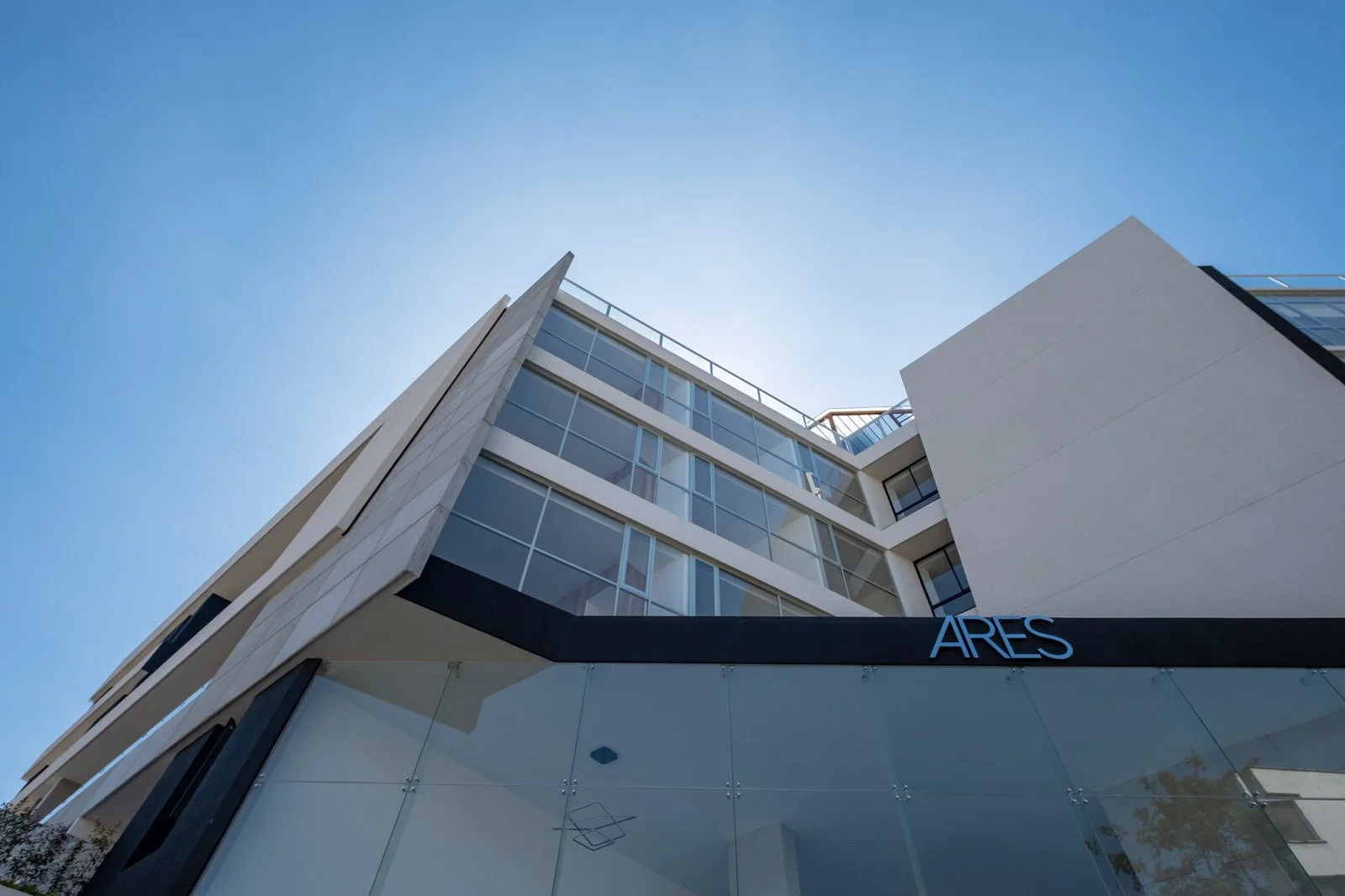 Edificio moderno de múltiples pisos con grandes ventanas y el signo 'ARES' en la fachada, bajo un cielo despejado.