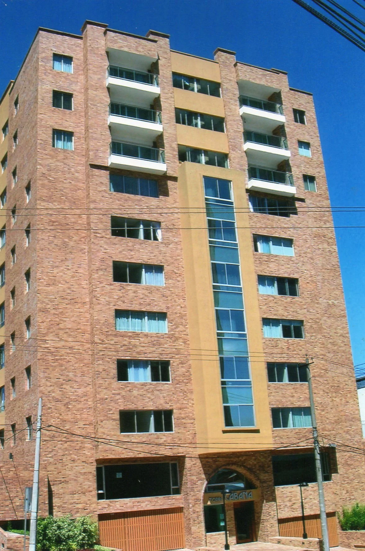 Edificio residencial de varios pisos con fachada de ladrillo y ventanas, en un día soleado con cielo azul.