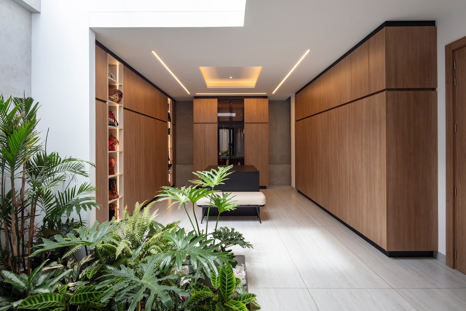 Vestíbulo moderno con paredes y mobiliario de madera, plantas verdes, sillón y puerta de madera.