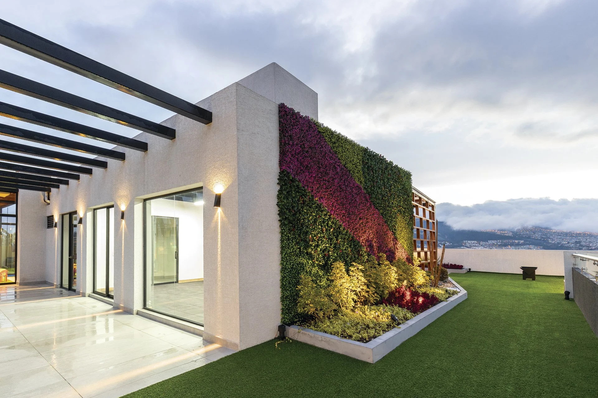 Terraza en un edificio moderno con muro de flores decorativas y entorno urbano en el fondo.