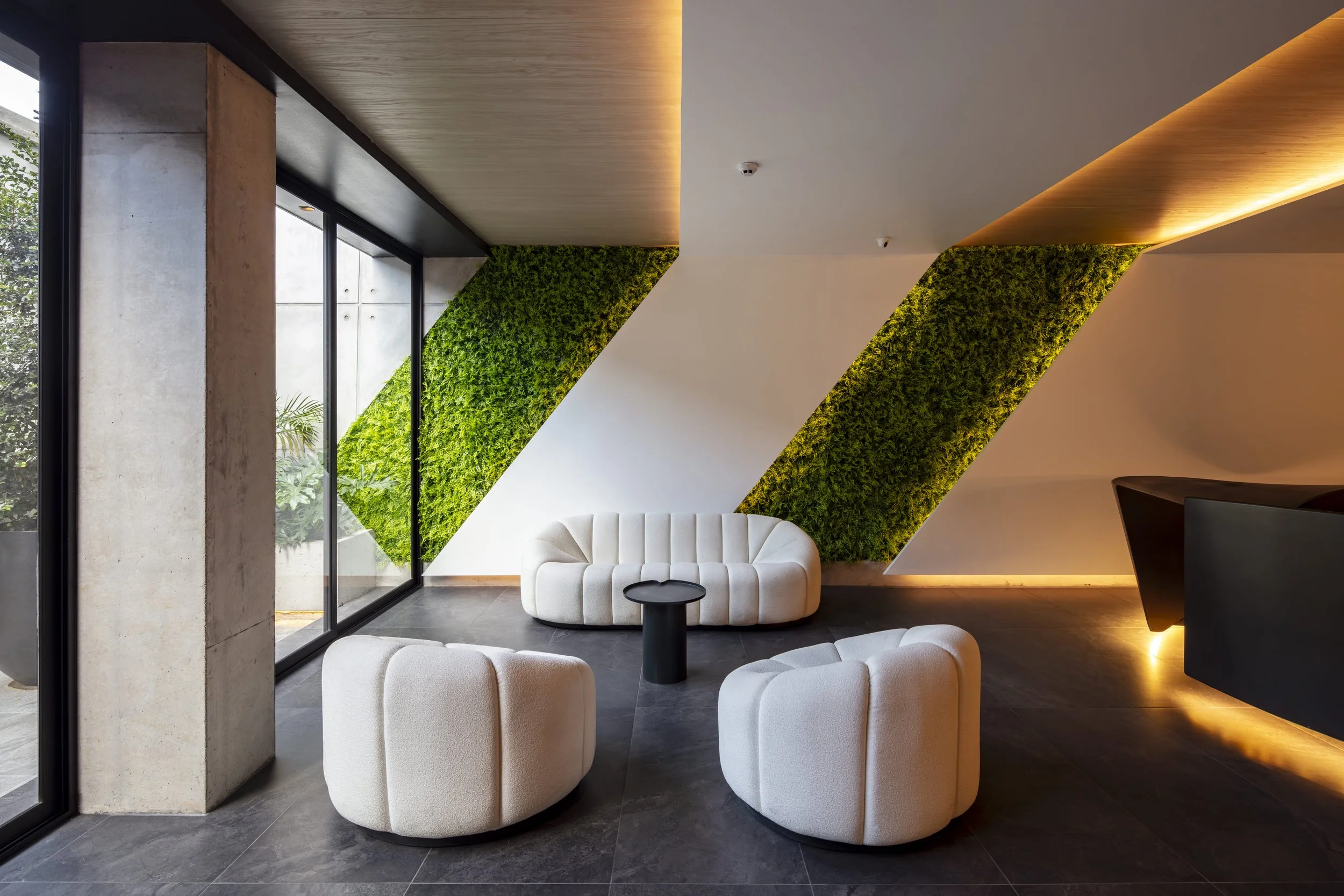 Quito, Ecuador es una Sala de interiores modernos de sala con sillones blancos, paredes con vegetación y grandes ventanas.