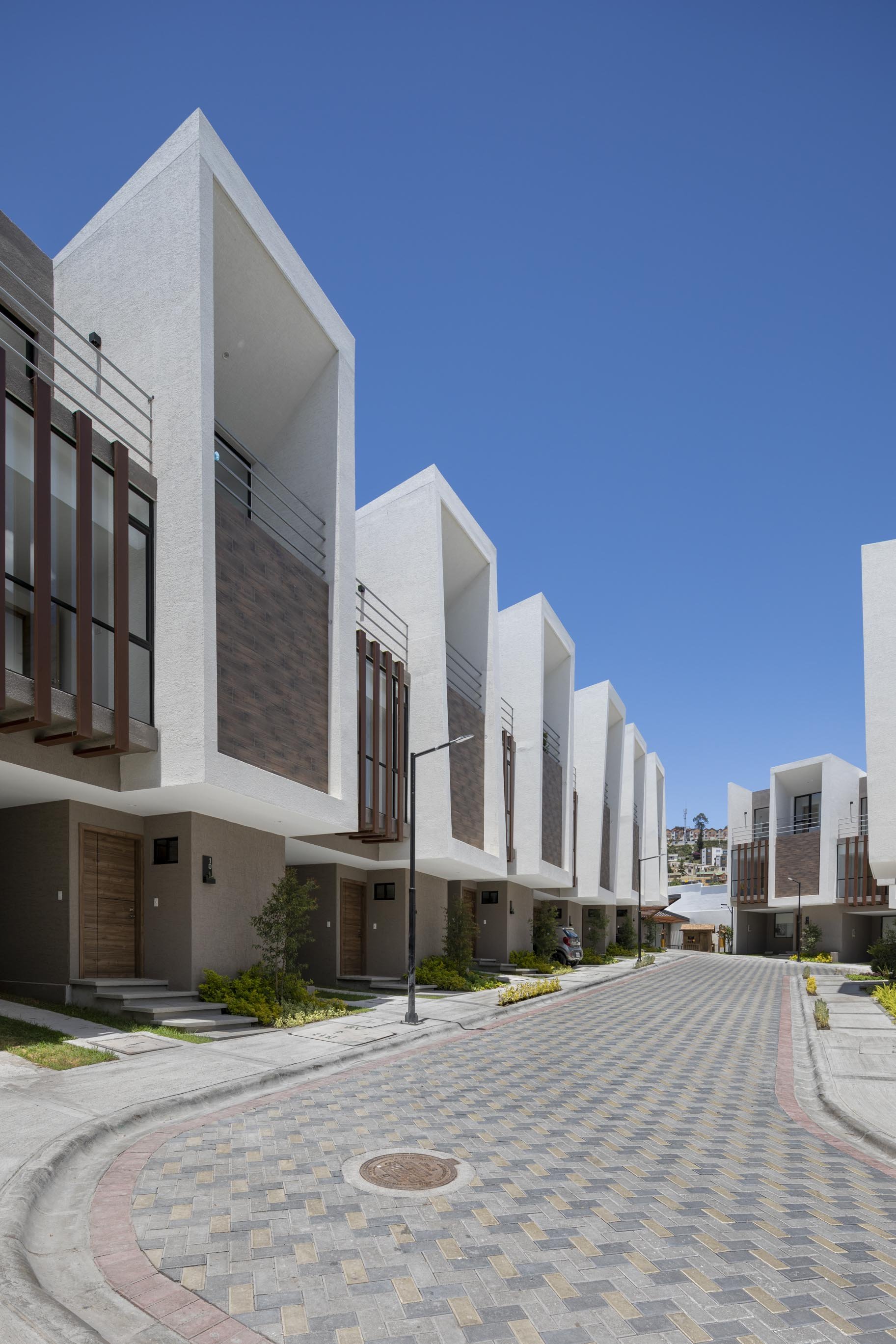 Conjunto de casas modernas de arquitectura minimalista en un barrio tranquilo con calle adoquinada y cielo despejado.
