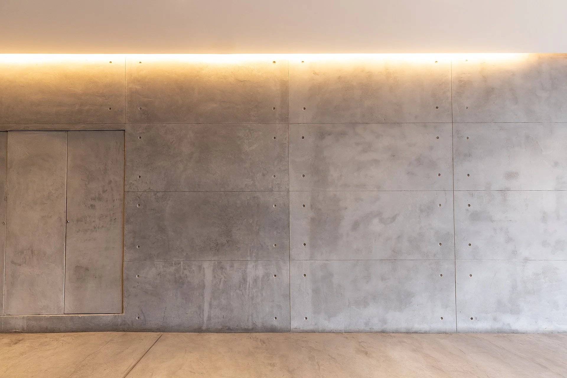 Pared de concreto con pequeñas perforaciones y iluminación en la parte superior.