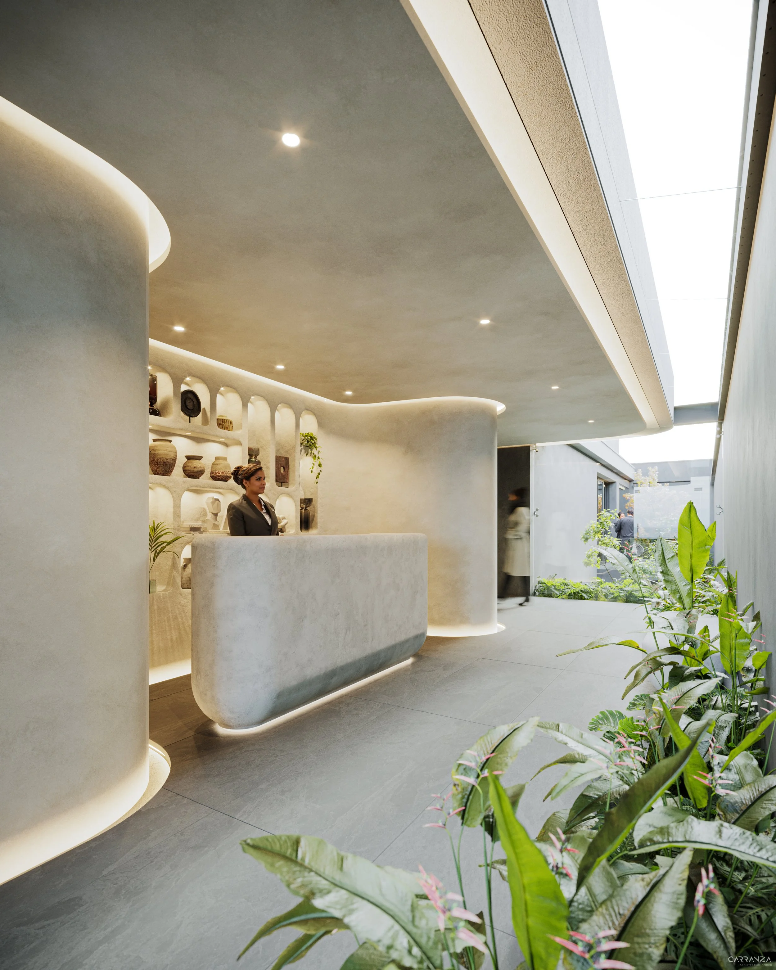 Recepción moderna con mostrador curvo, paredes y techo en tonos claros, estanterías con cerámicas decorativas, plantas verdes, luz cálida y un área exterior con vegetación.